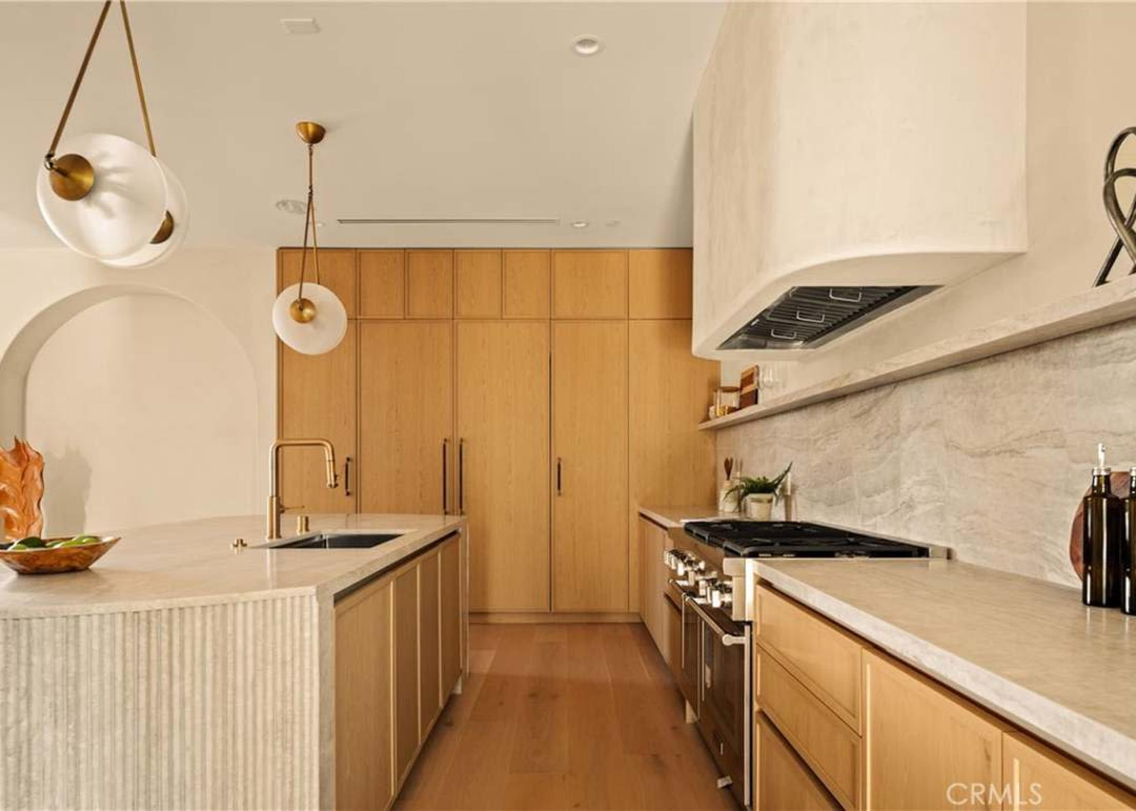 The kitchen features light wood cabinetry, a marble island, and modern appliances against a neutral backdrop.
