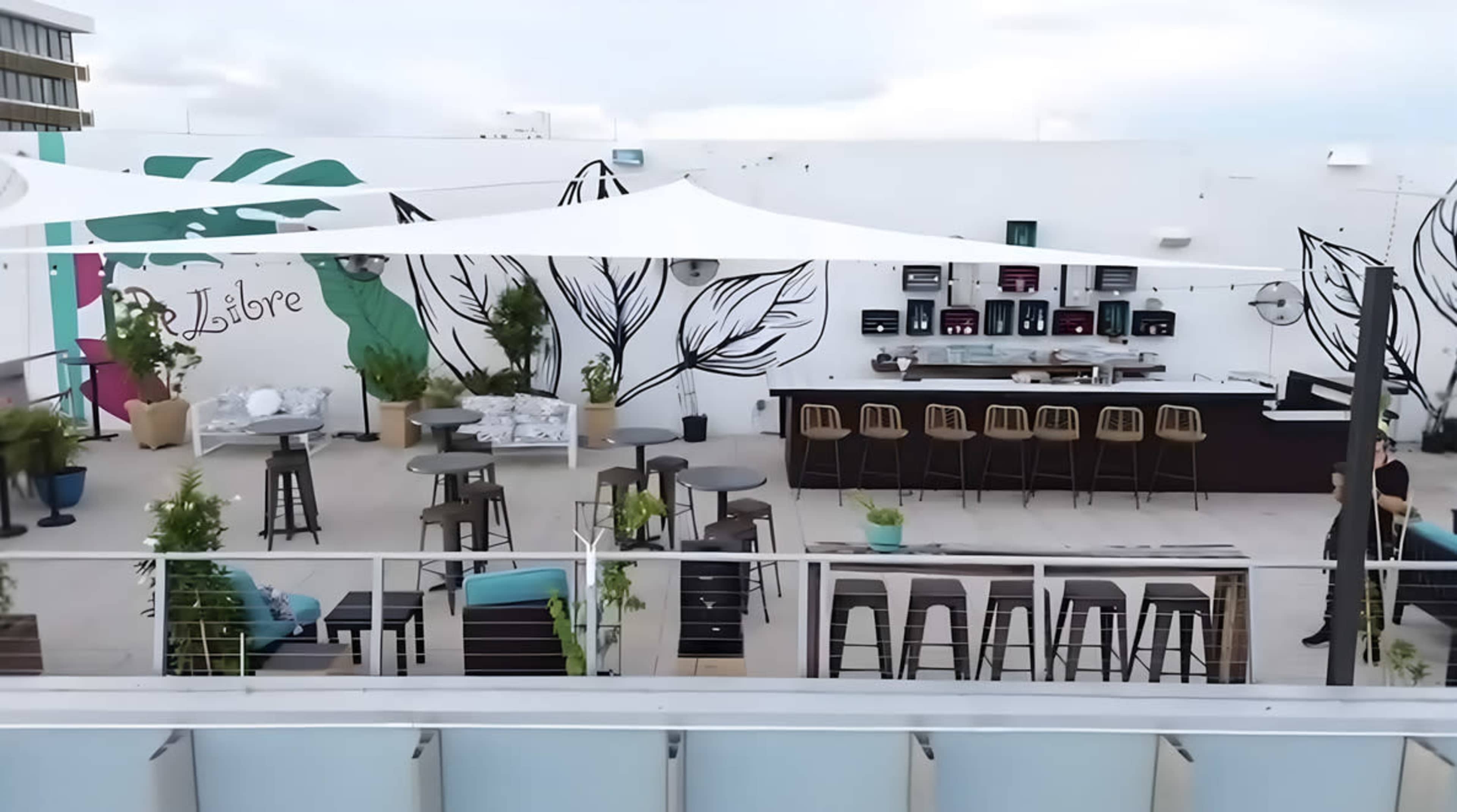 The image shows a rooftop terrace with modern furniture, a bar area, and large murals on the walls.