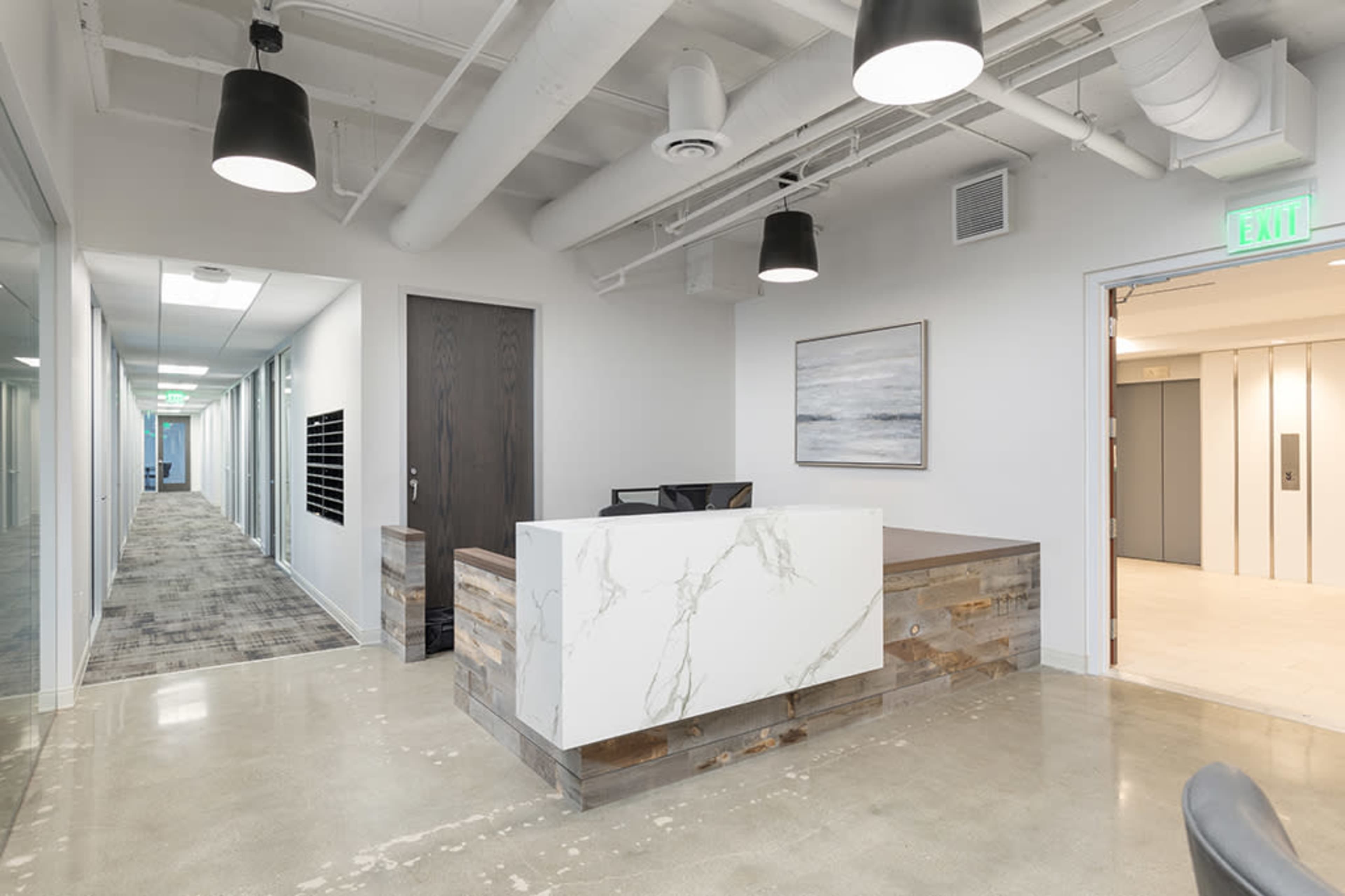 A modern office reception area with a marble-fronted desk, gray walls, and a hallway leading to various offices.