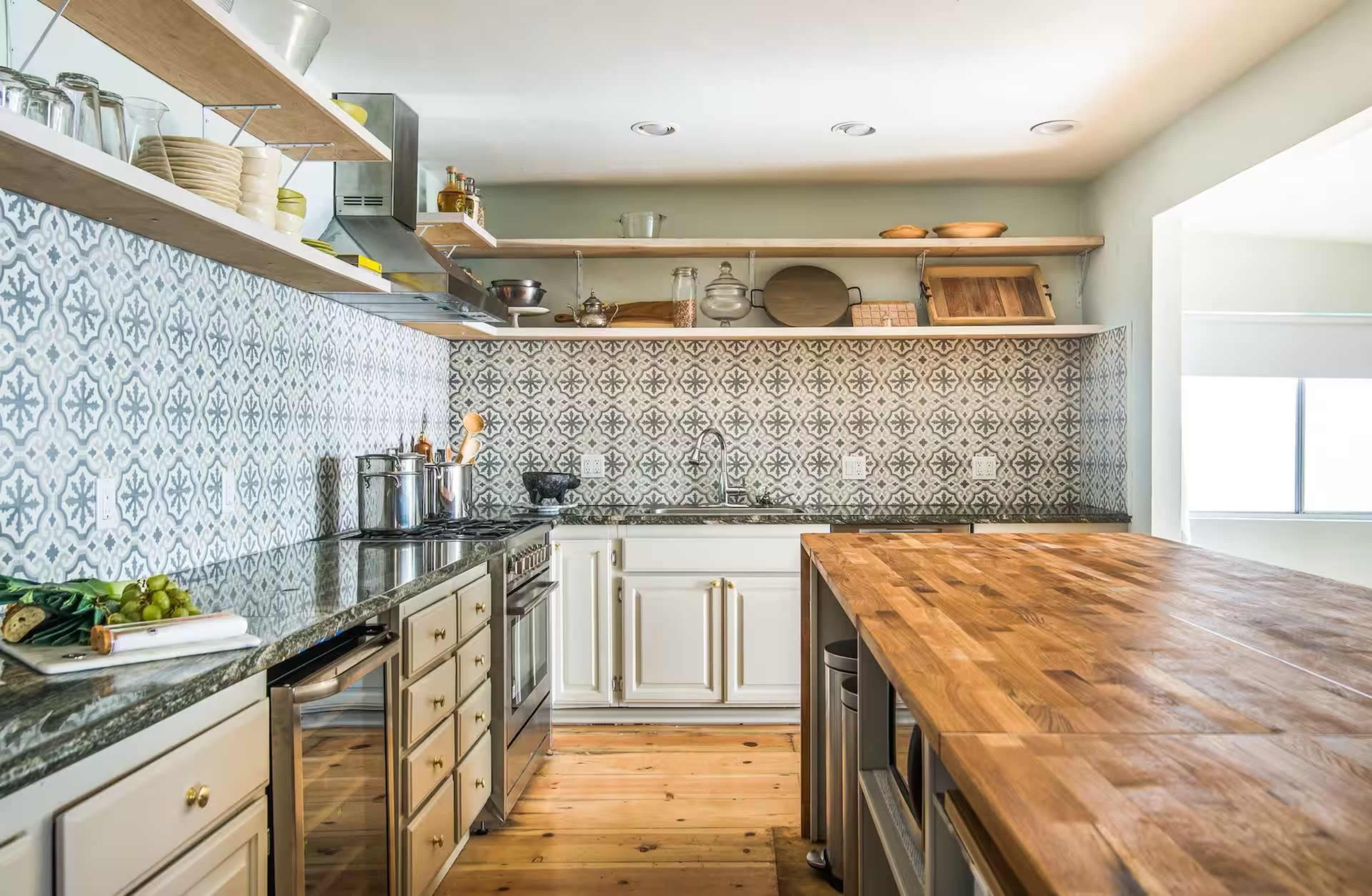 The image shows a modern kitchen with a wooden island, stainless steel appliances, and patterned tile on the walls.