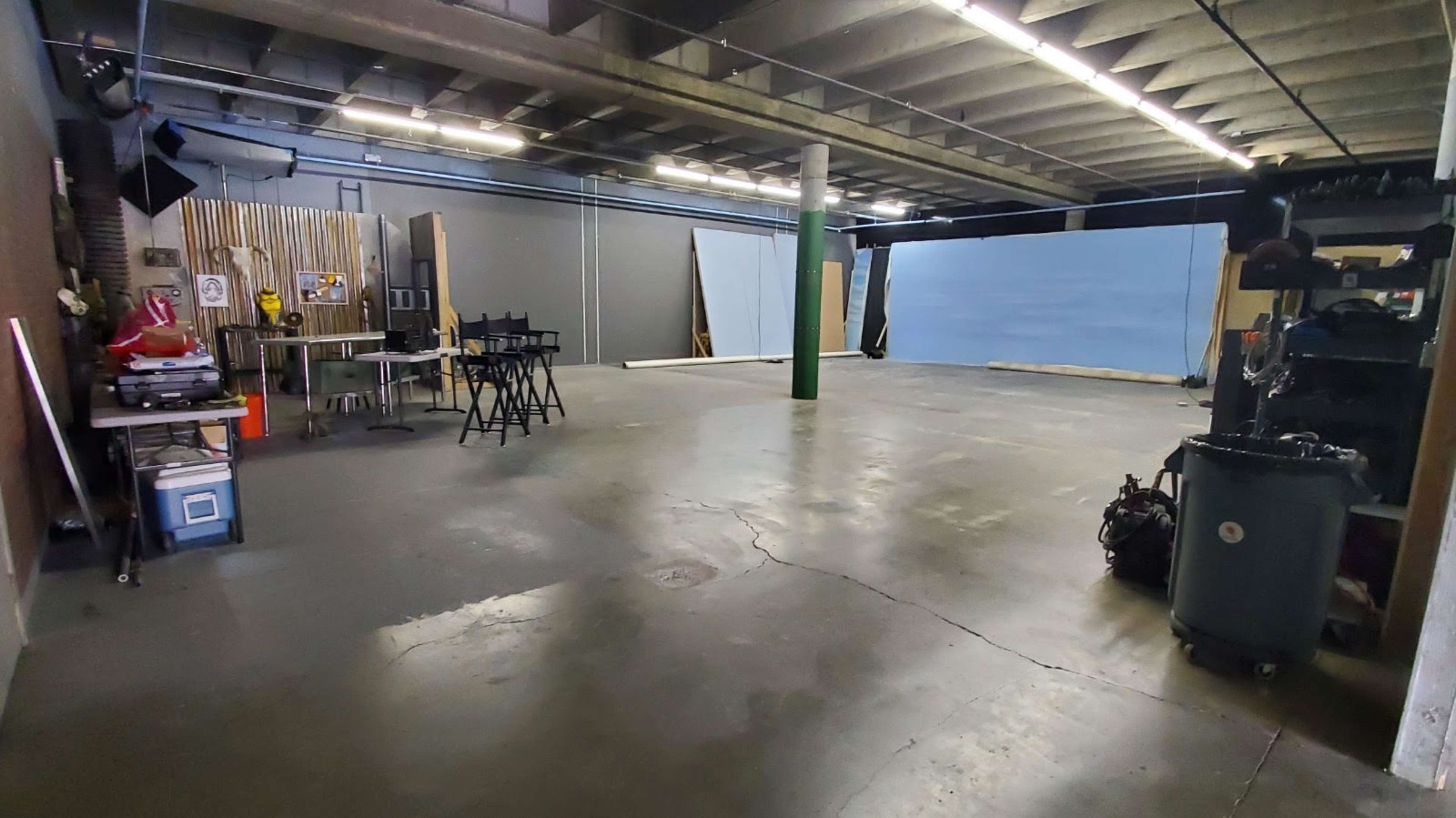A spacious, empty studio area with concrete flooring, equipped with various props and backdrops along one wall.