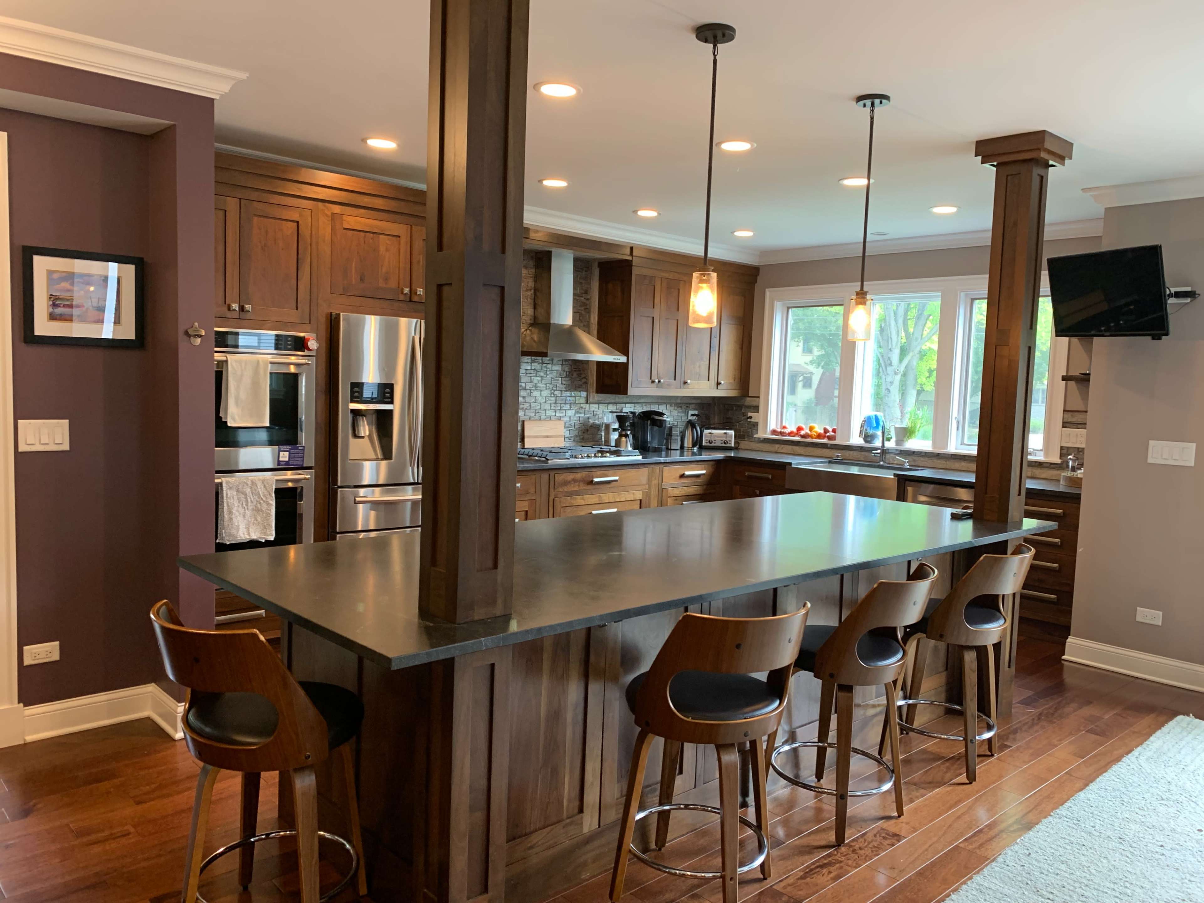 A modern kitchen with wooden cabinetry, a large island with seating for four, and stainless steel appliances.