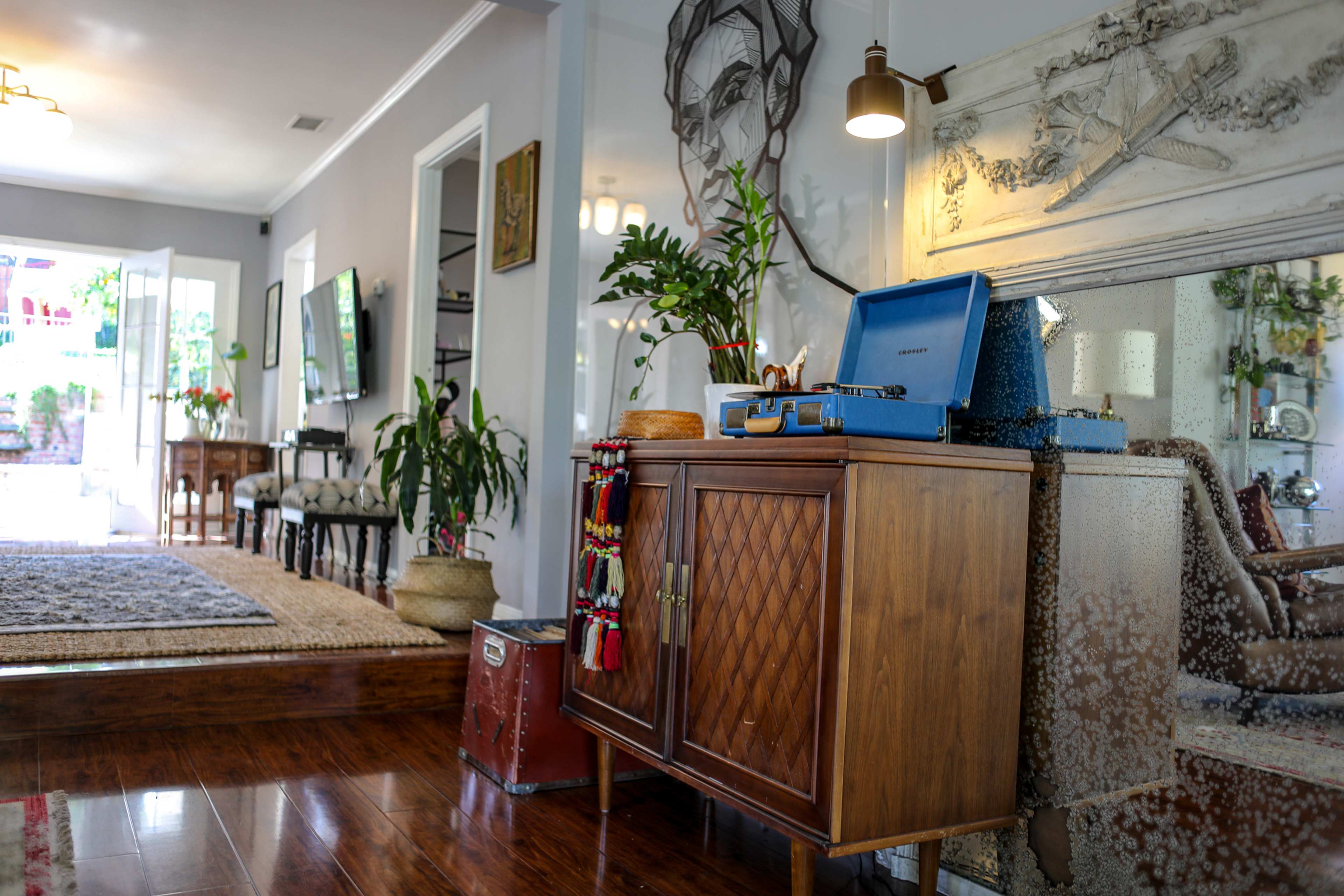 A cozy living room with wooden flooring, a retro turntable on a side cabinet, and a large mirror reflecting the space.