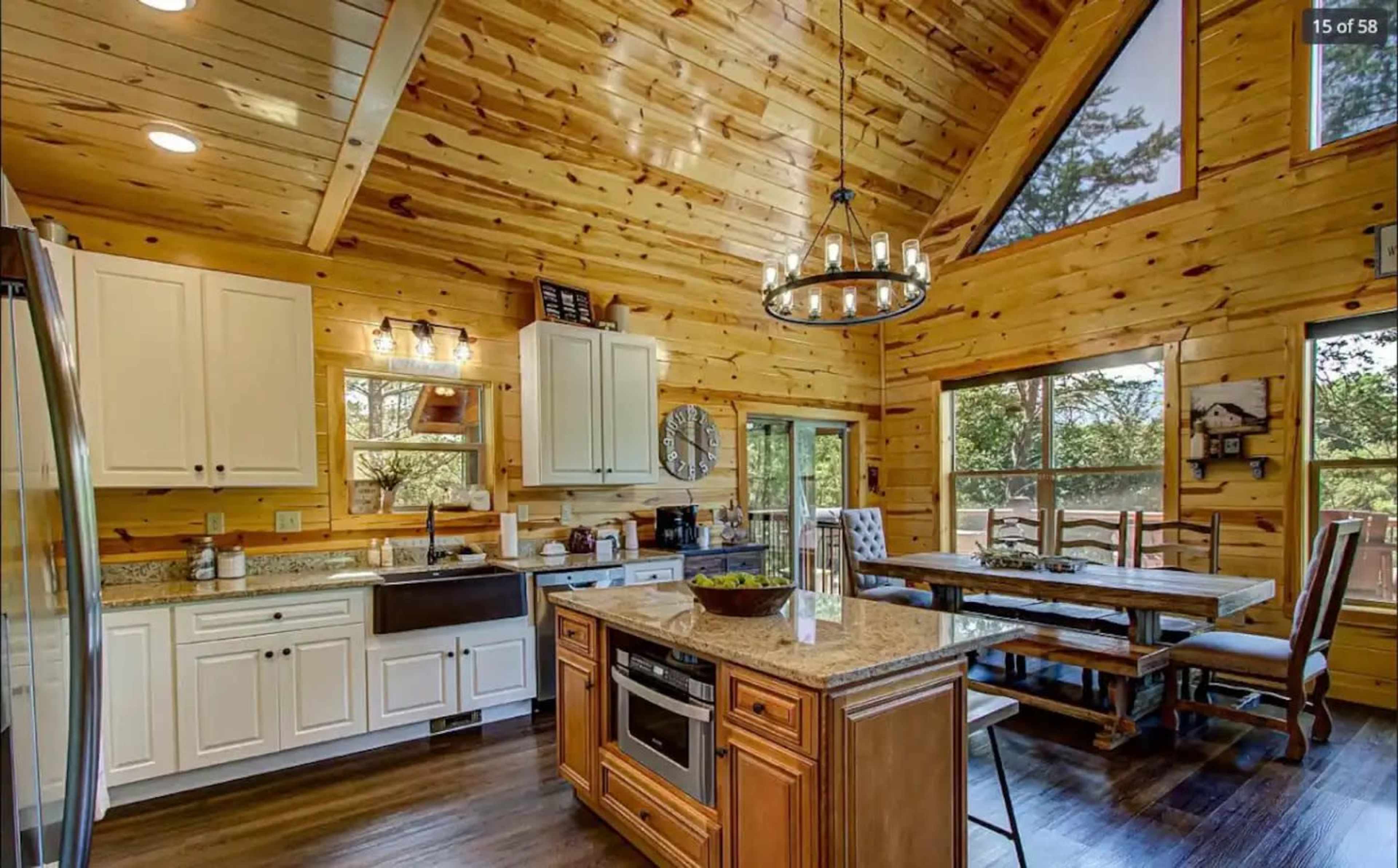 The image shows a spacious wooden kitchen and dining area featuring vaulted ceilings, a large island with a granite countertop, and a dining table near a window.
