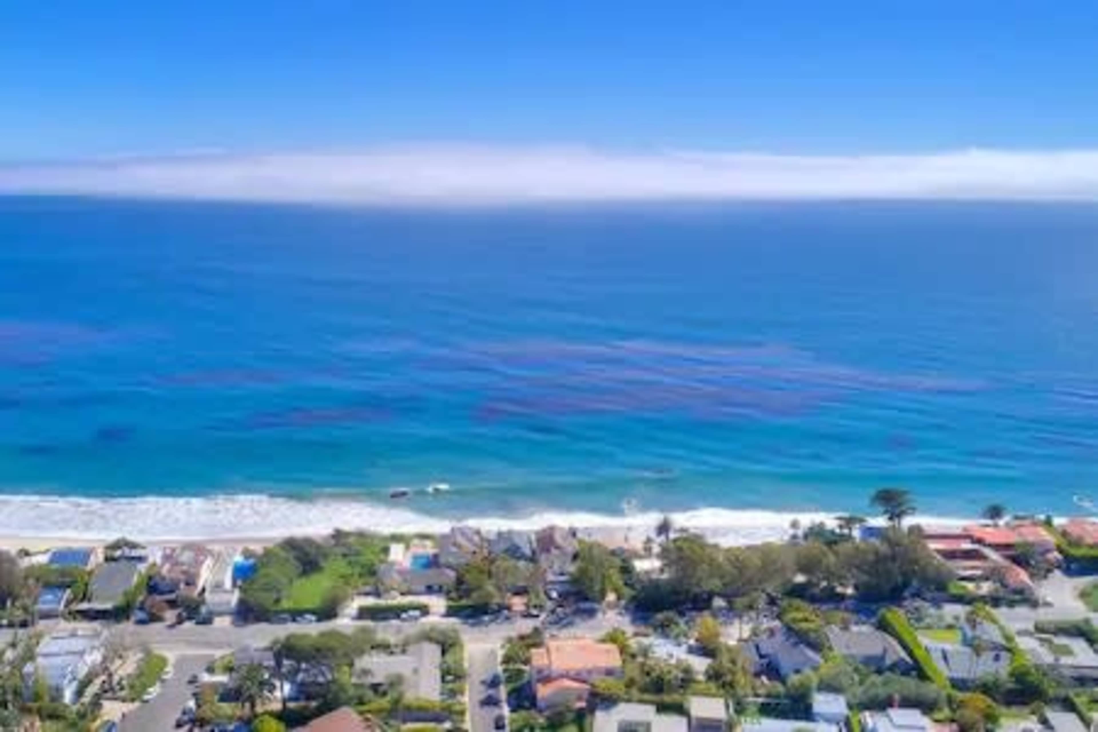 A coastal view with a line of houses alongside a sandy beach and clear blue ocean water.
