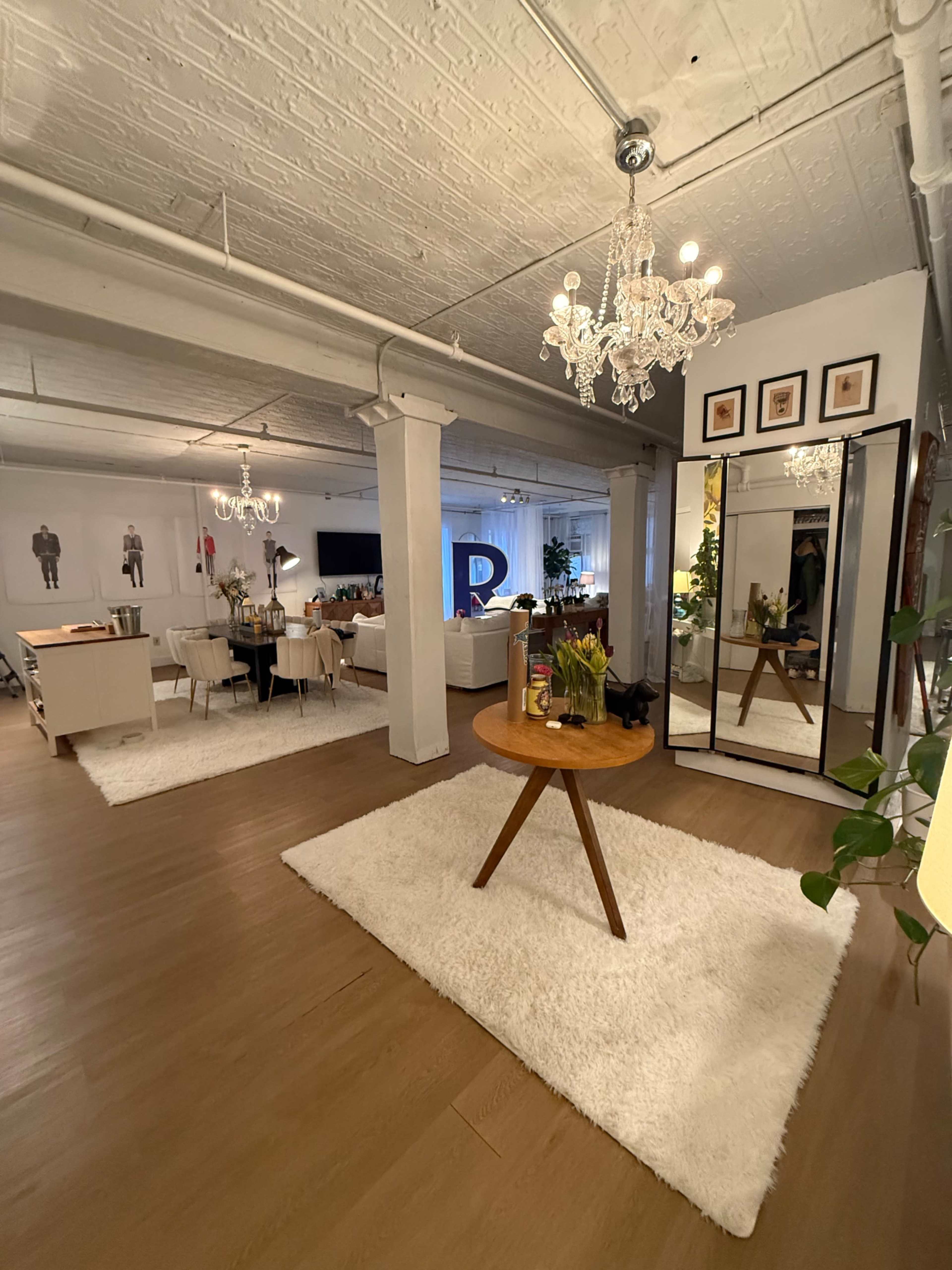 The image shows a spacious interior with a dining area, living room, and a large mirror on a wooden floor covered with a white rug.