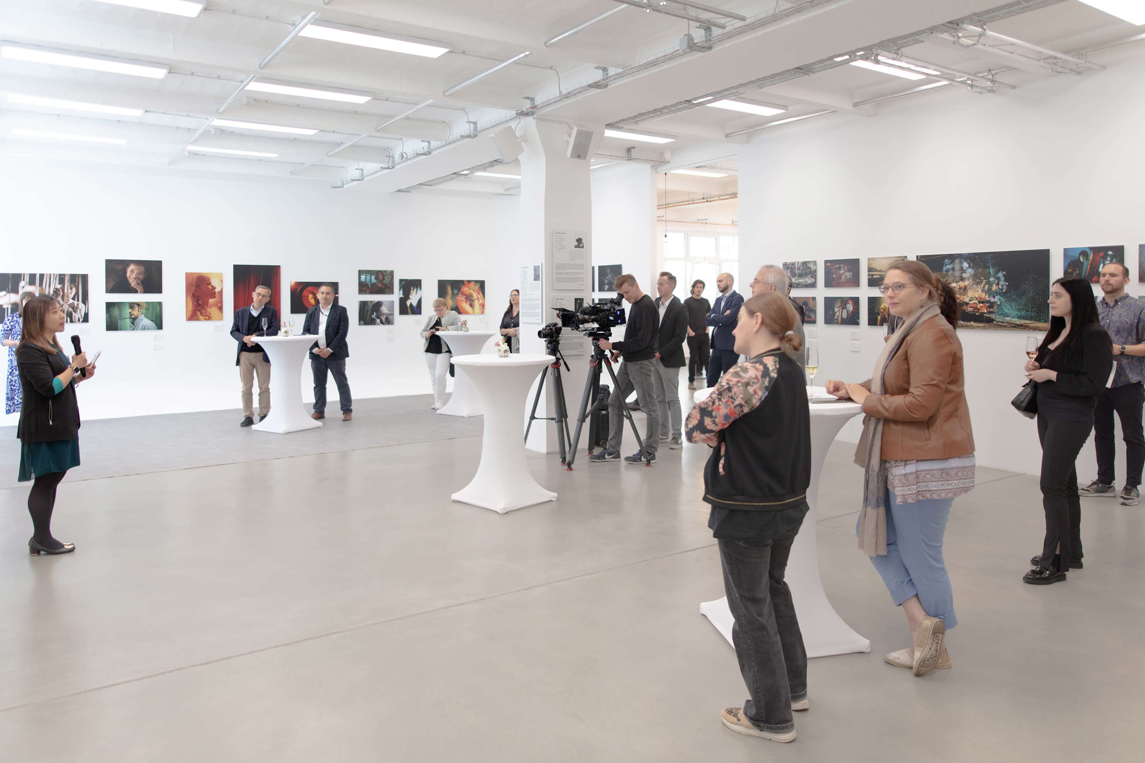 A group of people attends an art exhibition in a spacious gallery with several framed photographs displayed on the walls.