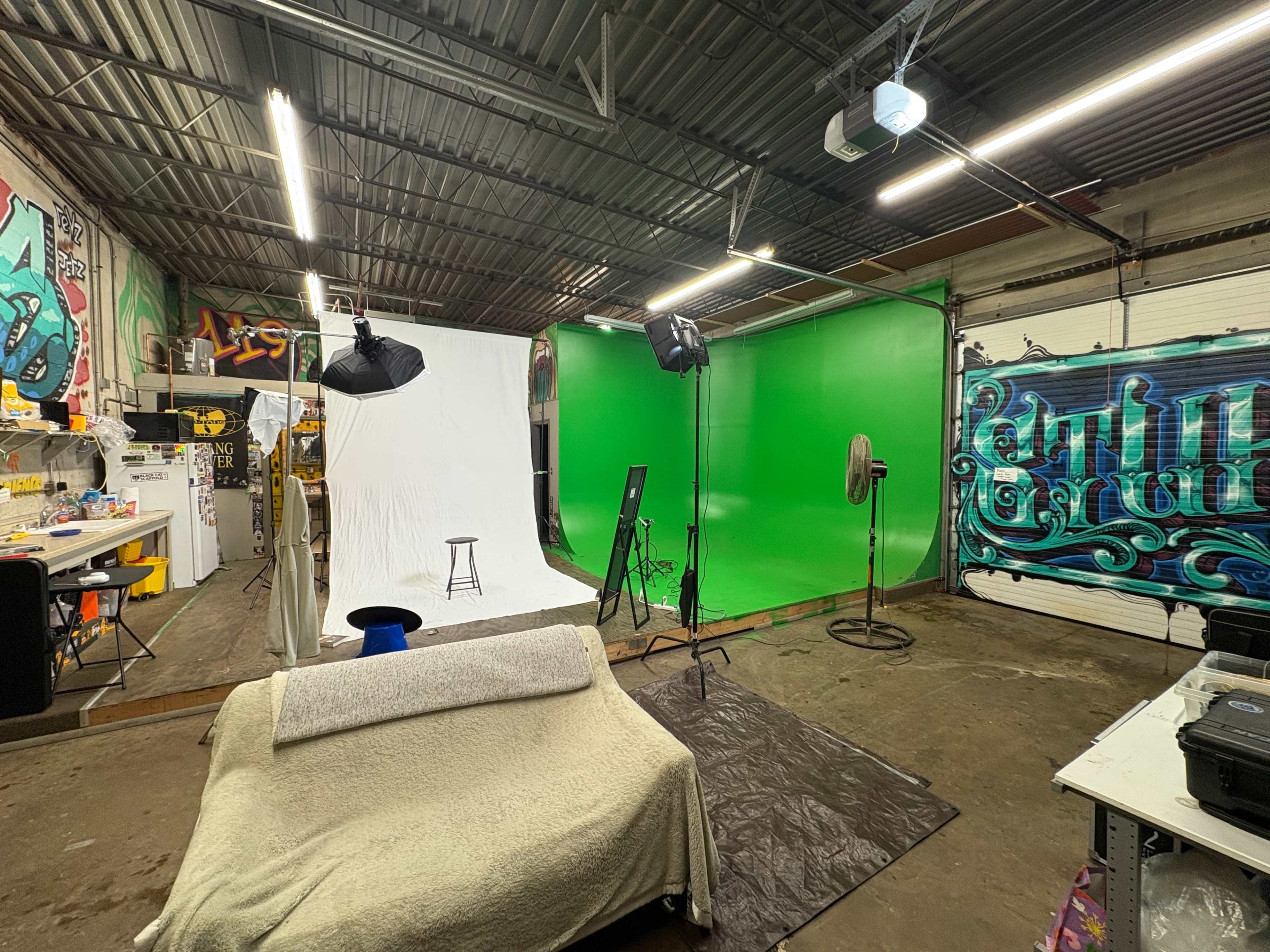 The image shows a spacious studio with a white backdrop, a green screen, various lighting equipment, and a sofa on a brown mat.