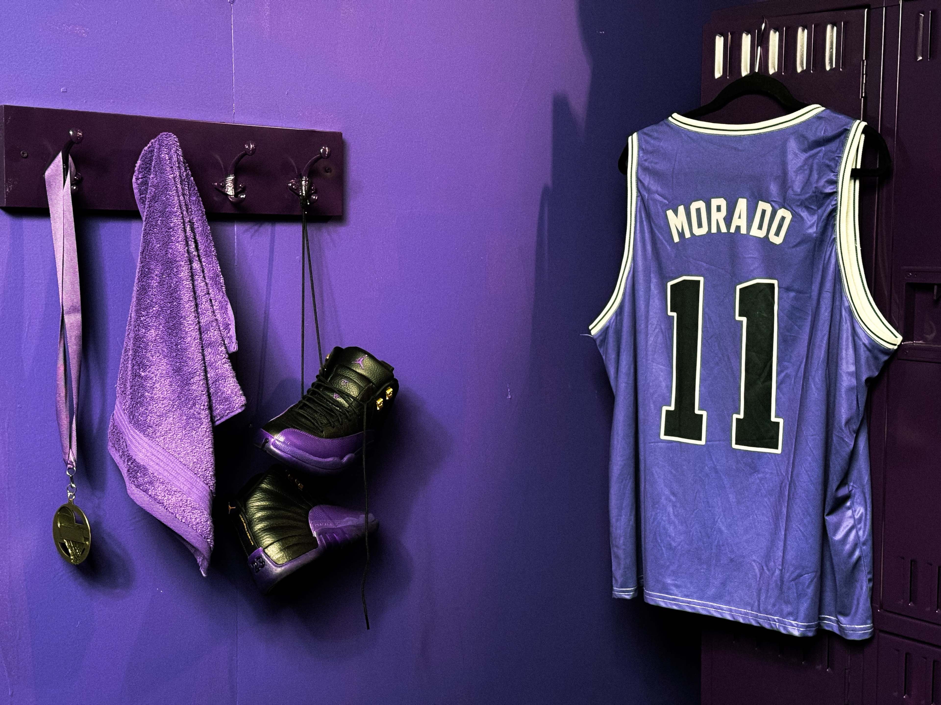 A purple-themed sports locker features a jersey labeled "Morado" with the number 11, a towel, a pair of shoes, and a medal hanging nearby.