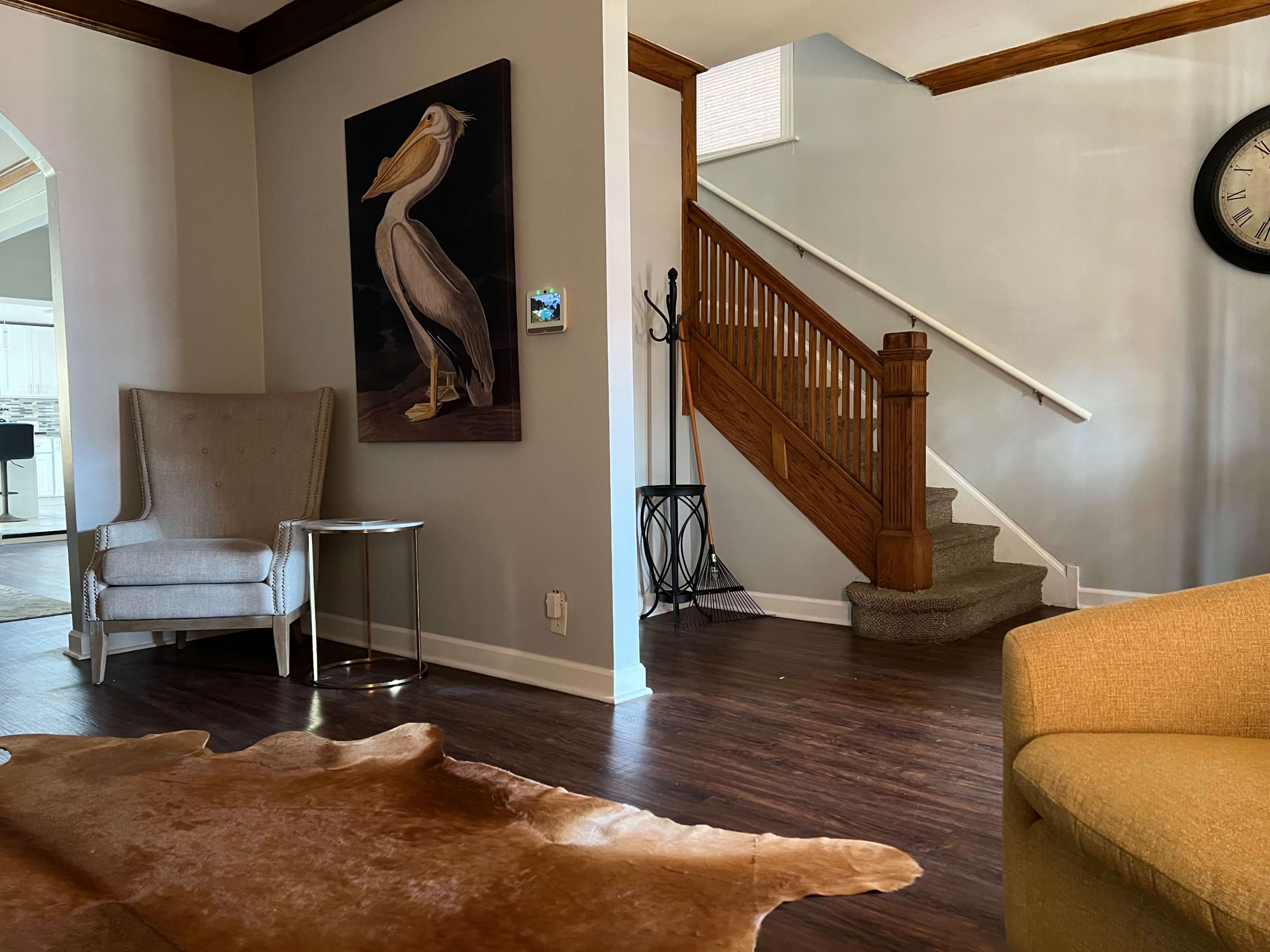 A living room area featuring a beige armchair and a yellow couch, with a wooden staircase leading to an upper level.