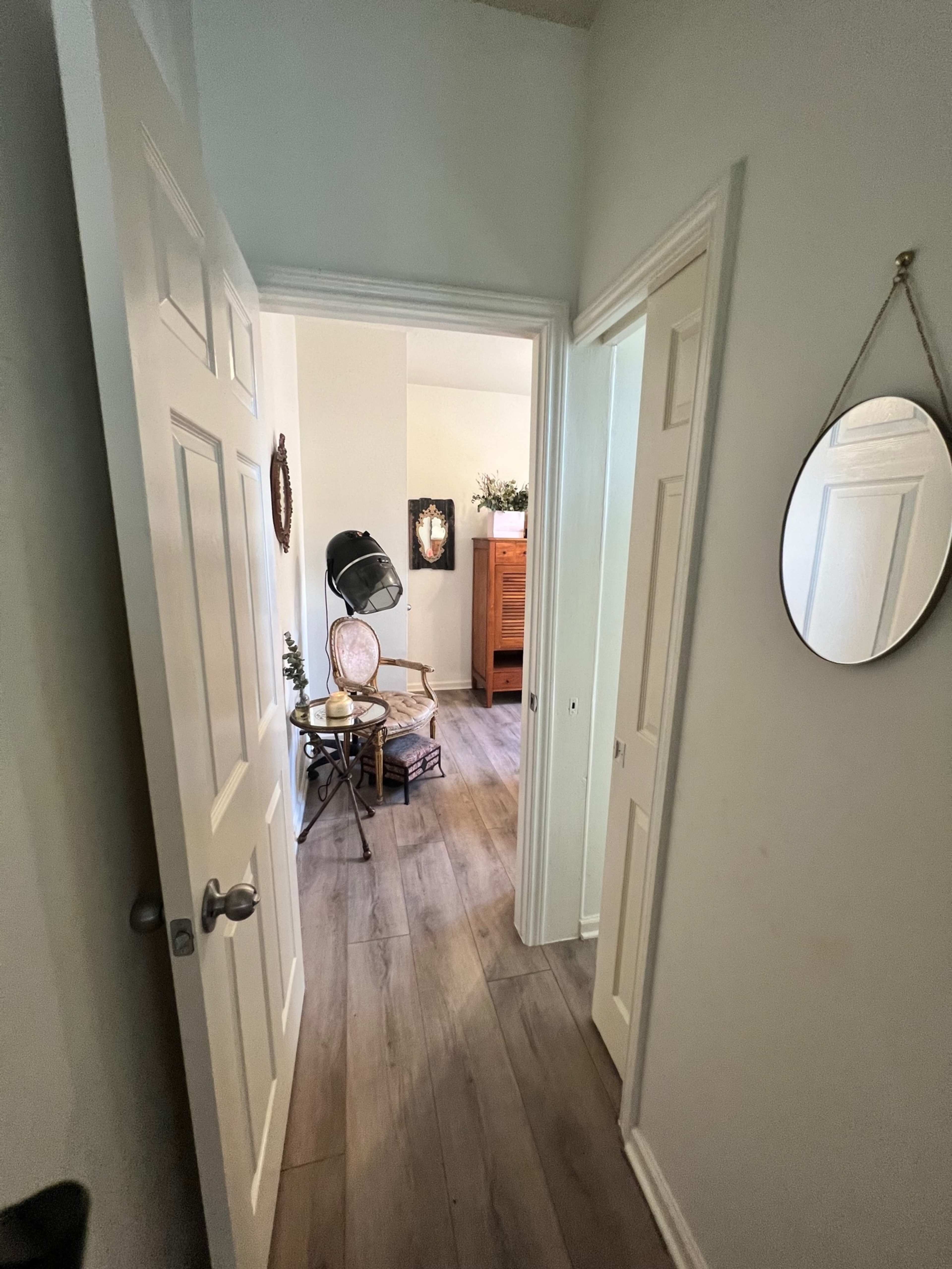 The image shows a hallway leading to a small, well-lit room with a chair and a standing lamp.