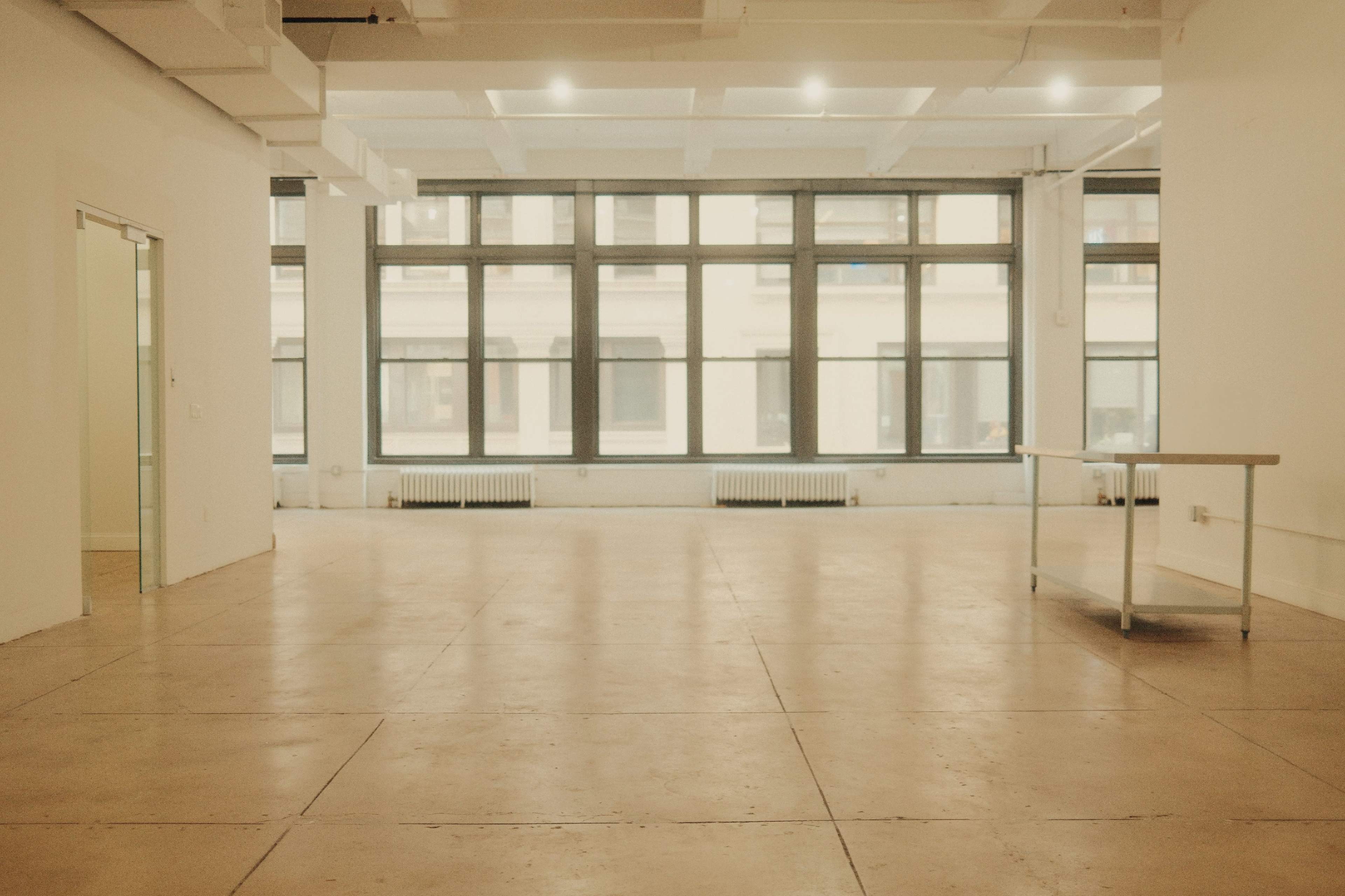 An empty workspace with concrete flooring and large windows allowing natural light to enter.