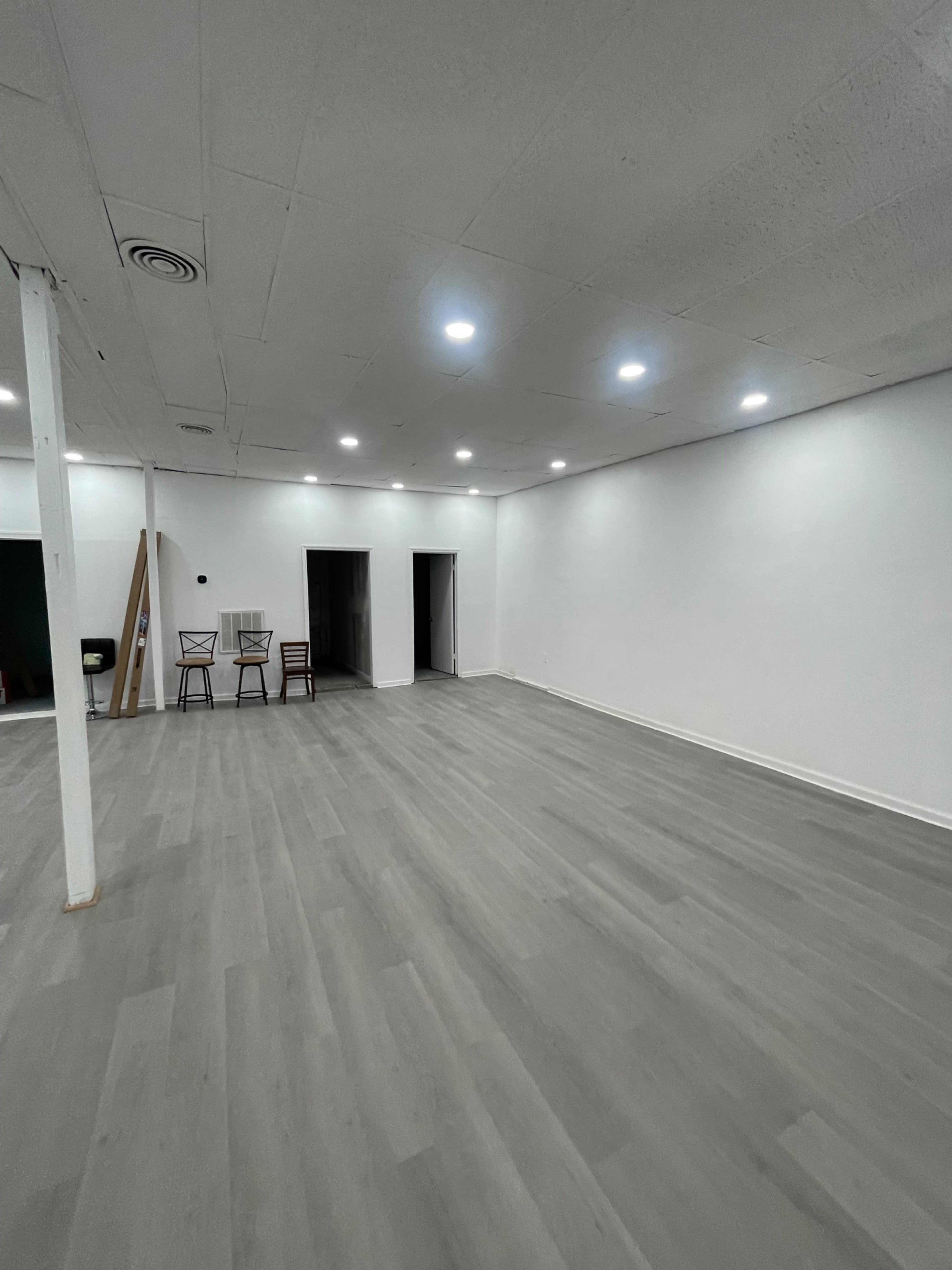 A spacious, empty room with gray flooring, white walls, and several overhead lights illuminating the area.