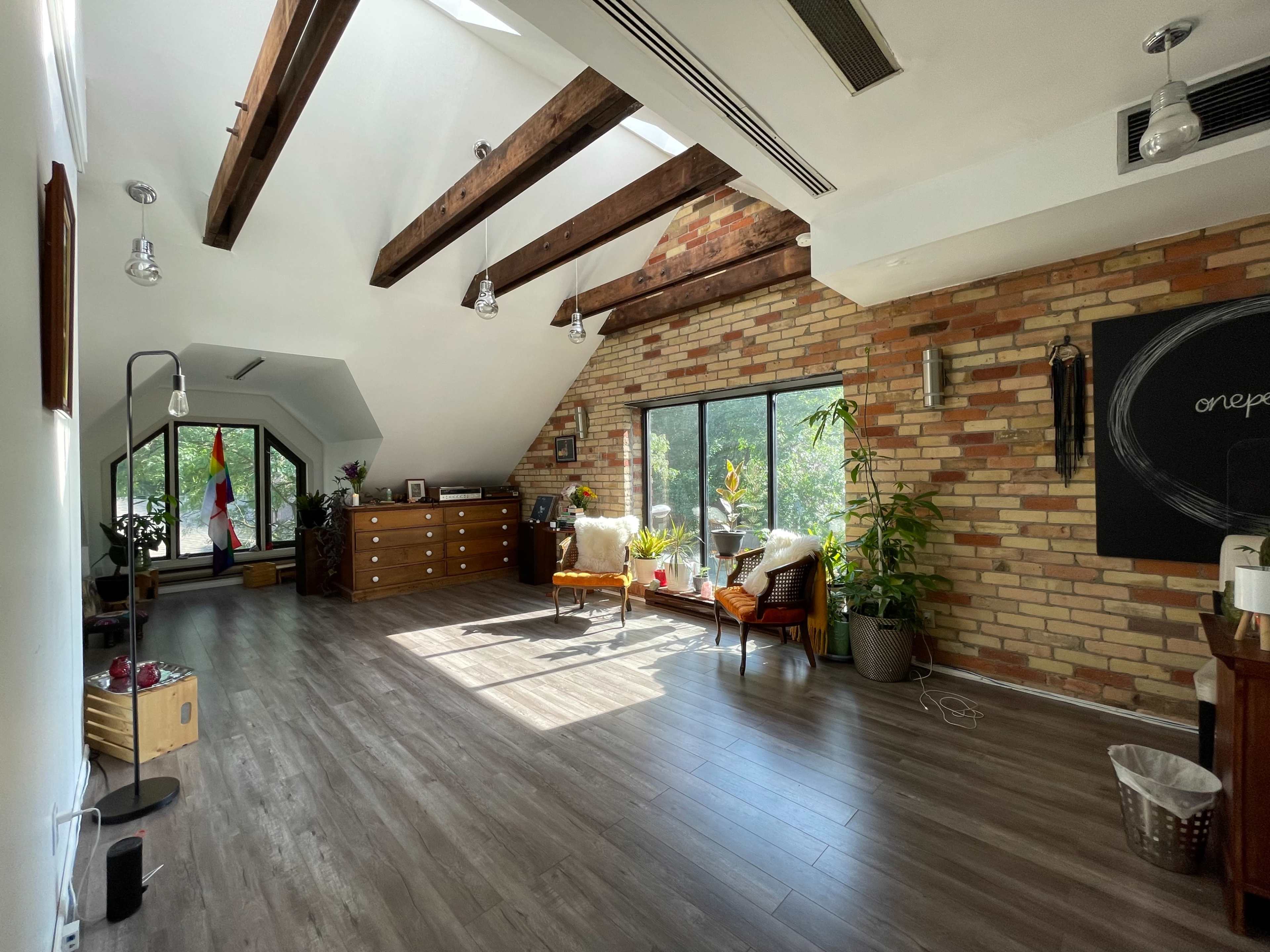 A spacious room with wooden beams, brick walls, large windows, and minimalist furniture.