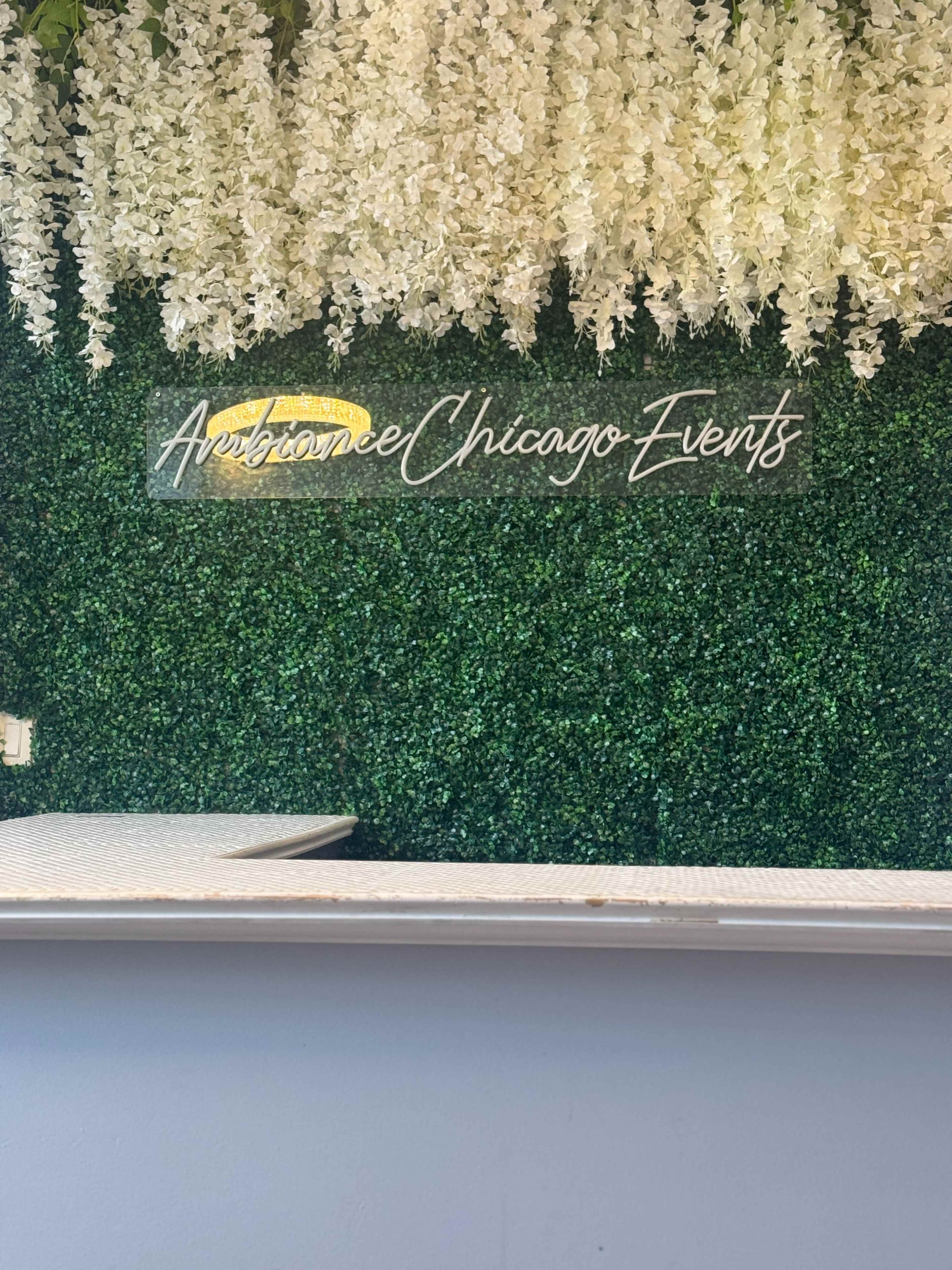 The image features a decorative green wall with artificial flowers and a sign that reads "Ambiance Chicago Events."