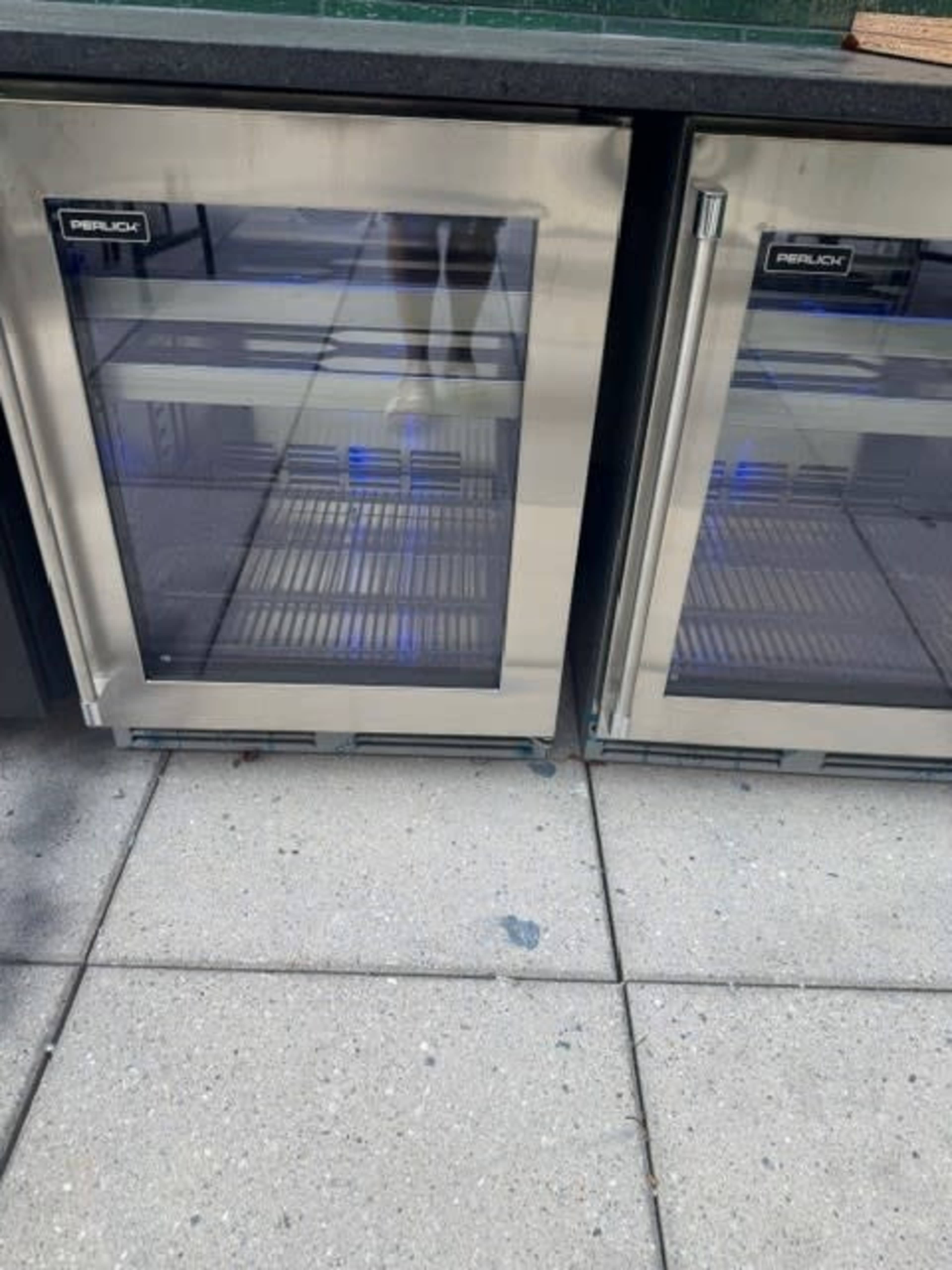 The image shows two stainless steel beverage refrigerators with glass doors and blue interior lights, placed on a tiled surface.