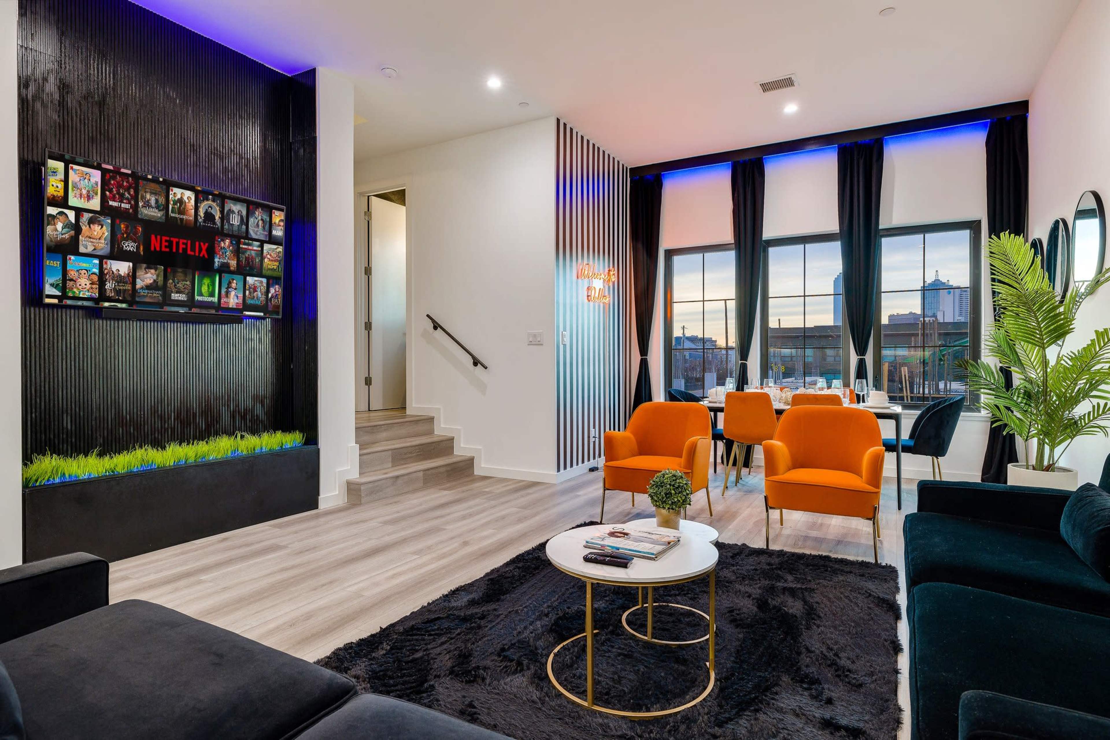 A modern living space featuring a black couch, orange chairs, a round coffee table, and a decorative wall with a TV displaying Netflix content.