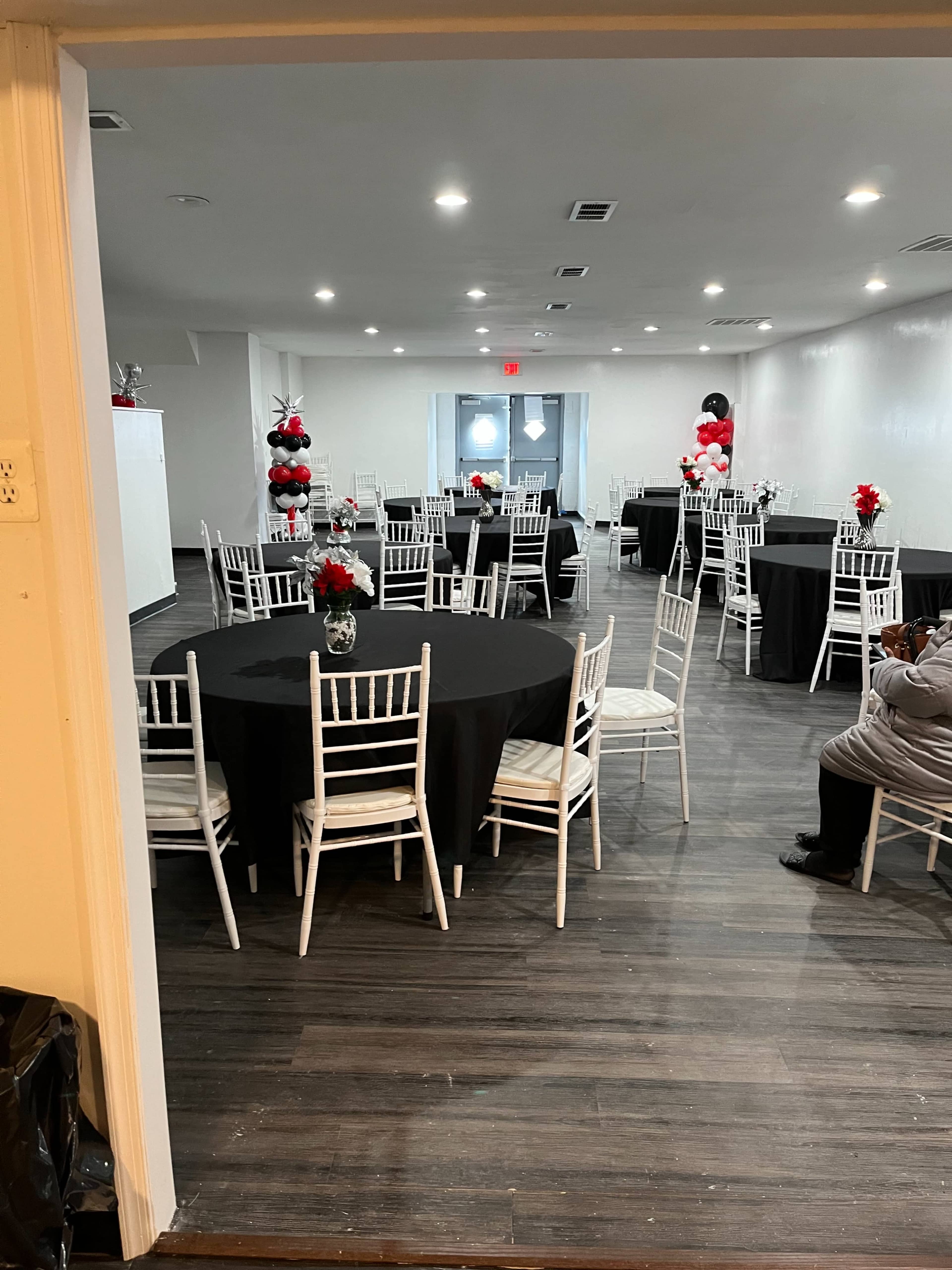The image shows a spacious event room with black and white tables decorated with red and white floral centerpieces.
