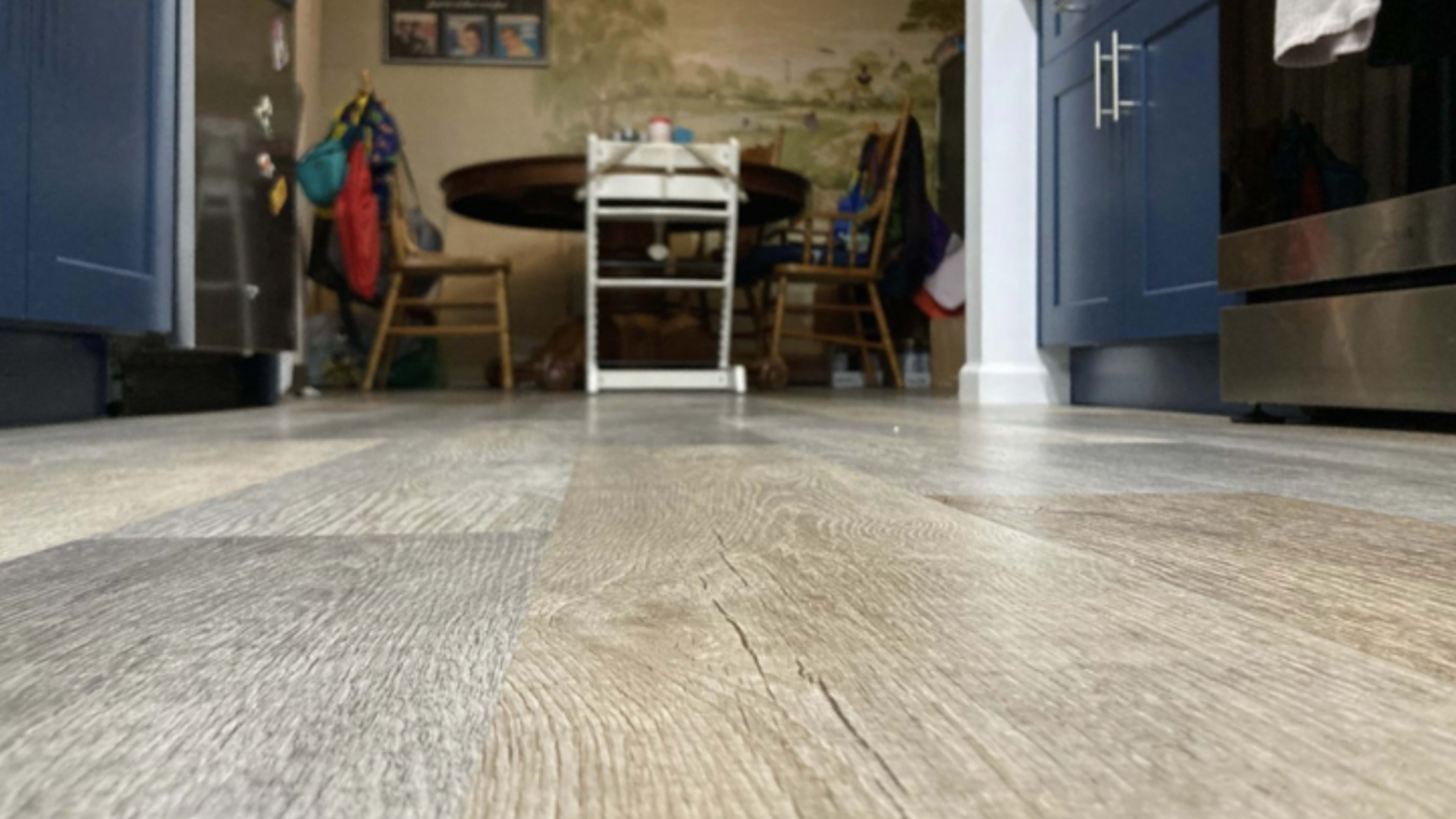 A kitchen floor with wood-like laminate, leading toward a table and chairs in the background.