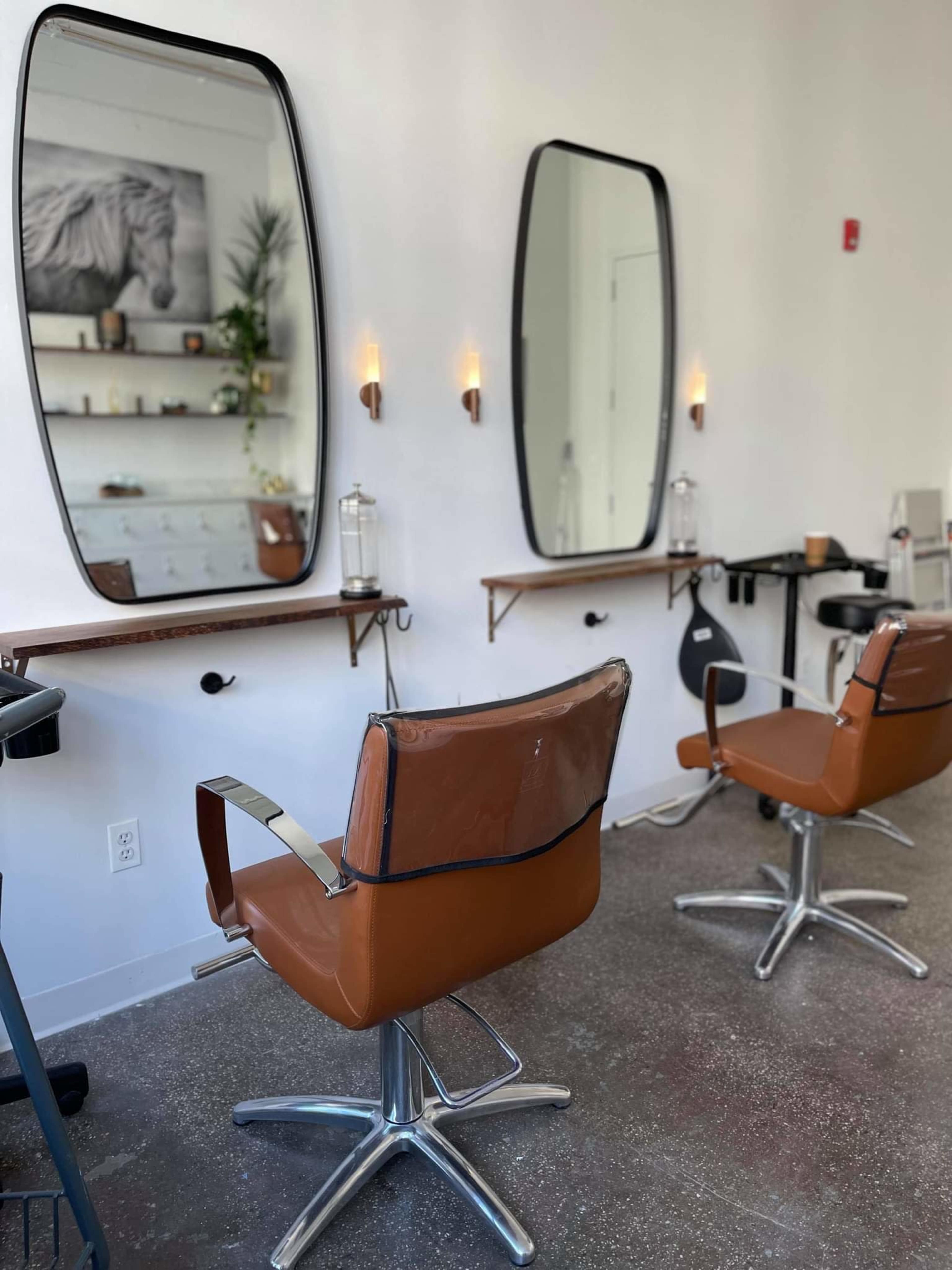 A minimalist hair salon with two brown salon chairs and large mirrors mounted on the wall.