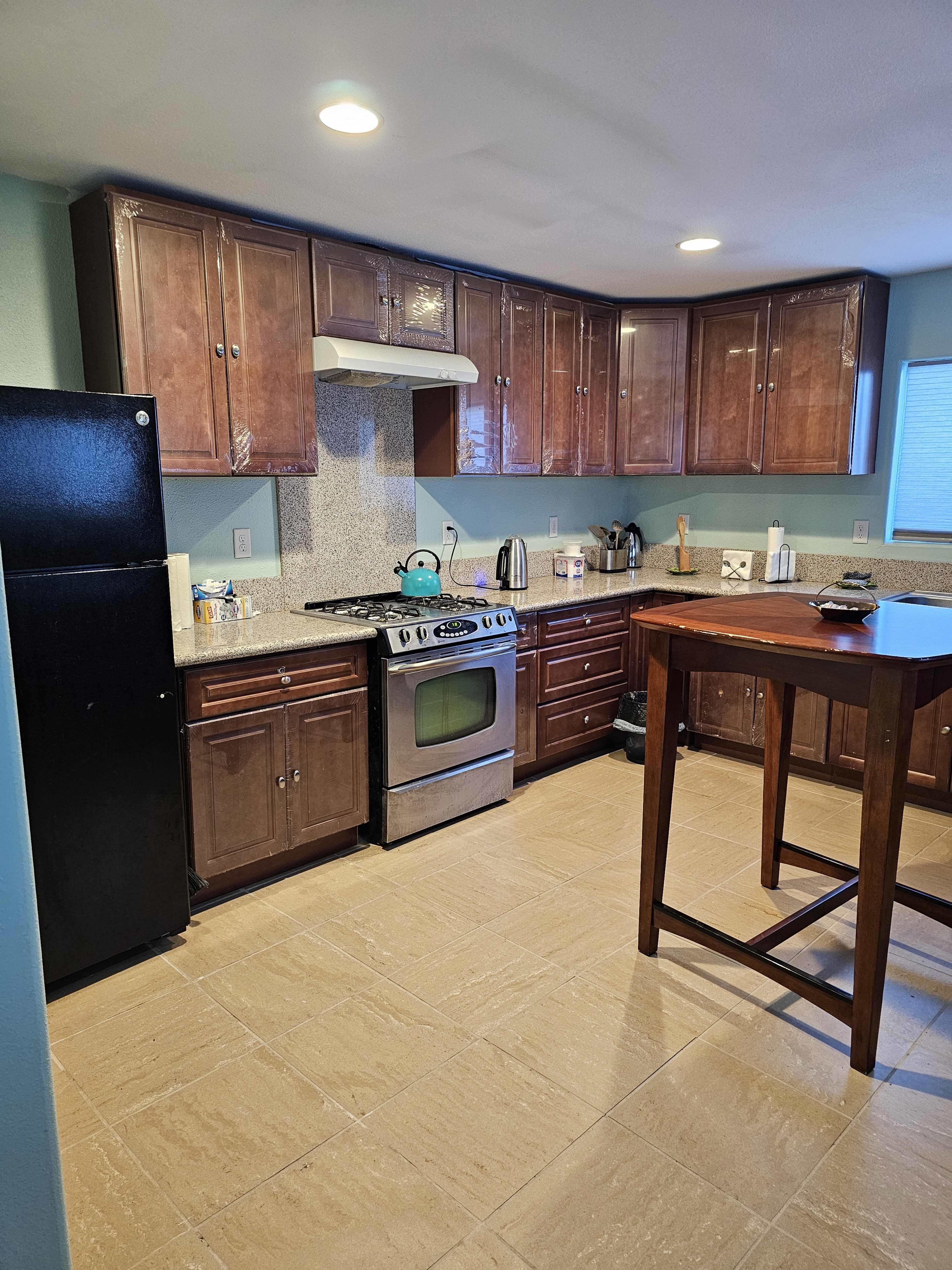 A kitchen with wooden cabinetry, a stainless steel stove, and a small wooden table in the center.