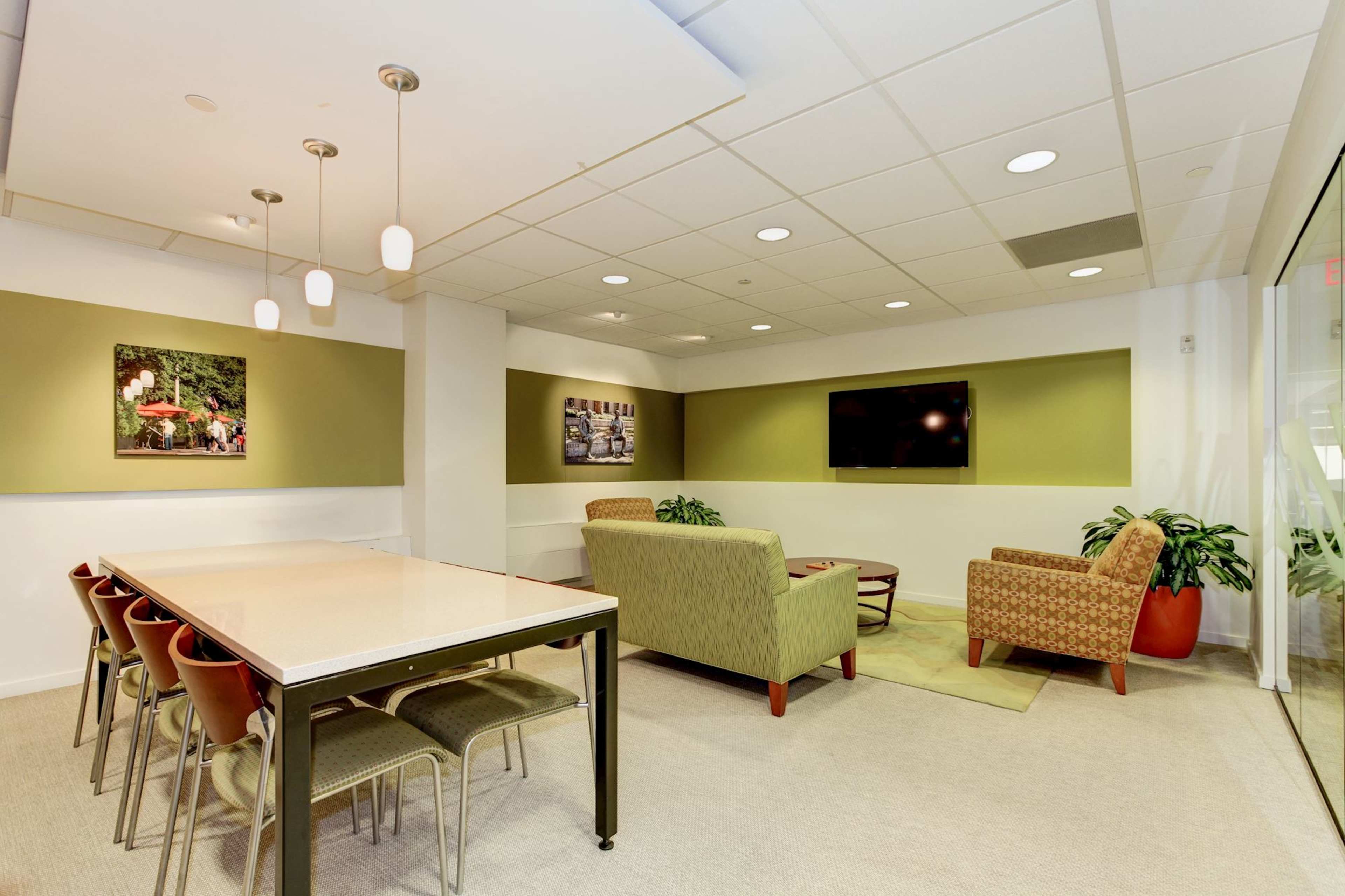A modern lounge area features a dining table with chairs, a seating arrangement, and wall-mounted artwork.