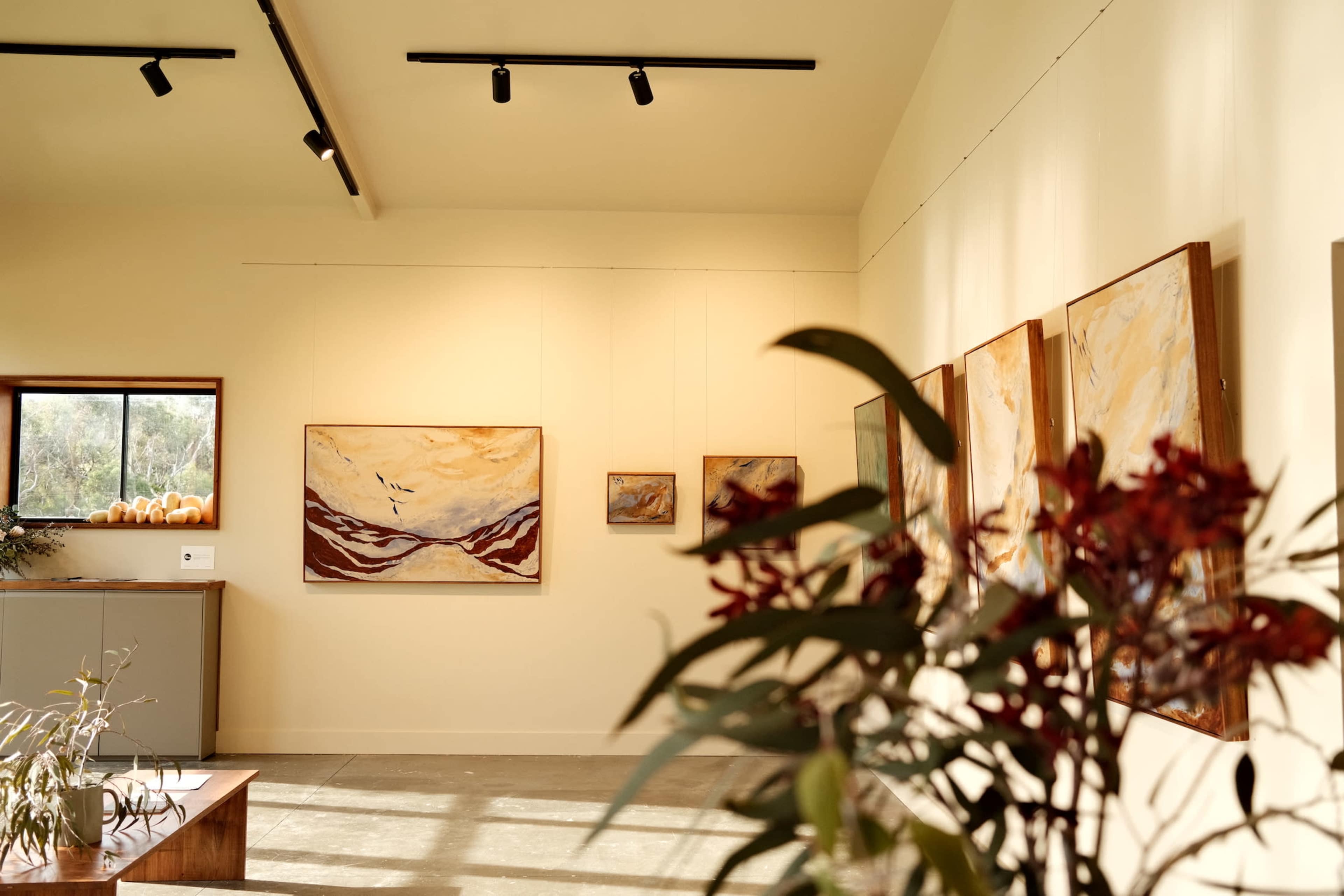 An art gallery displays a series of abstract paintings on the walls, with a view of a potted plant in the foreground.