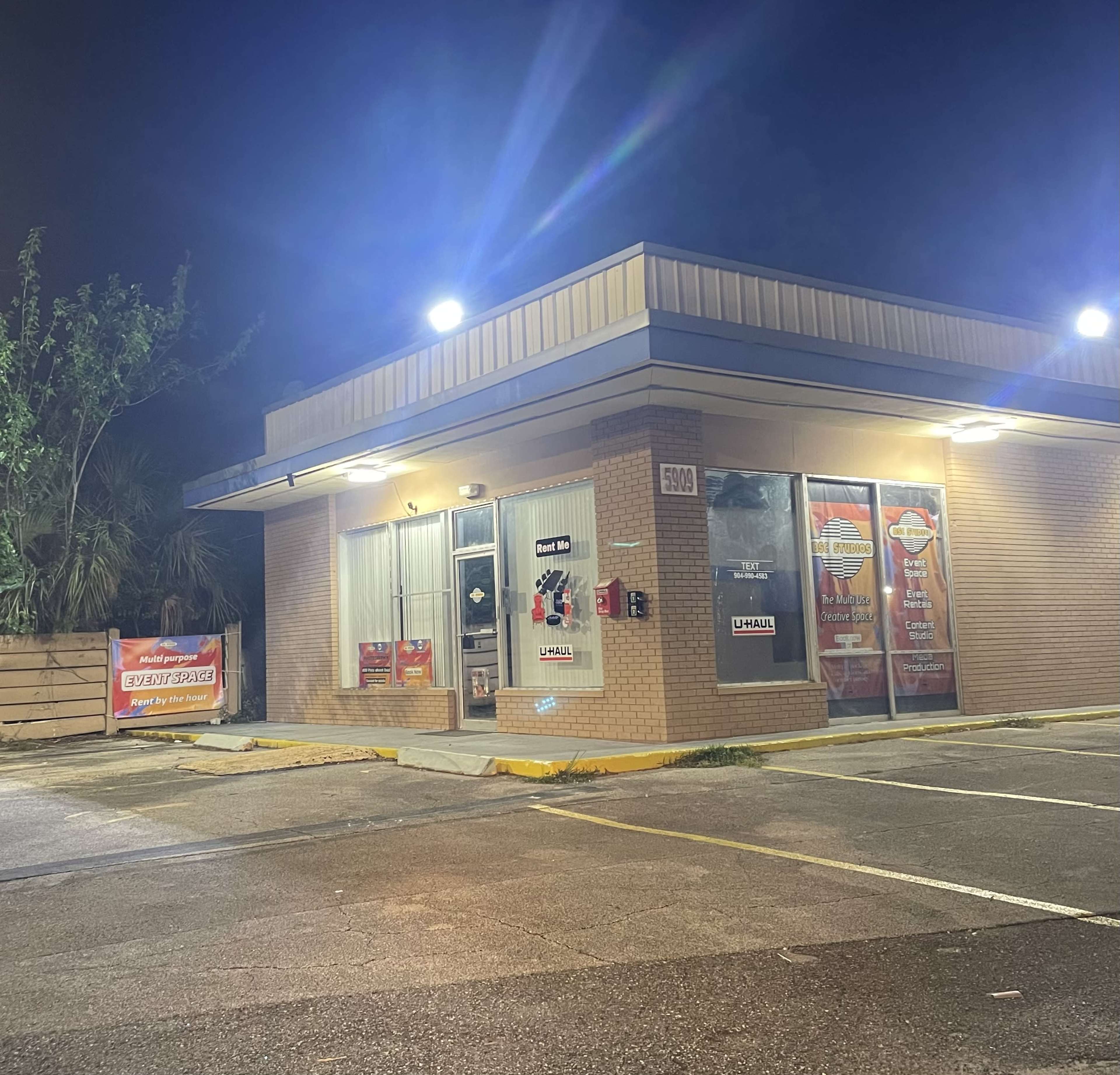 A vacant commercial building with illuminated signs stands at night, featuring large windows and a parking lot.
