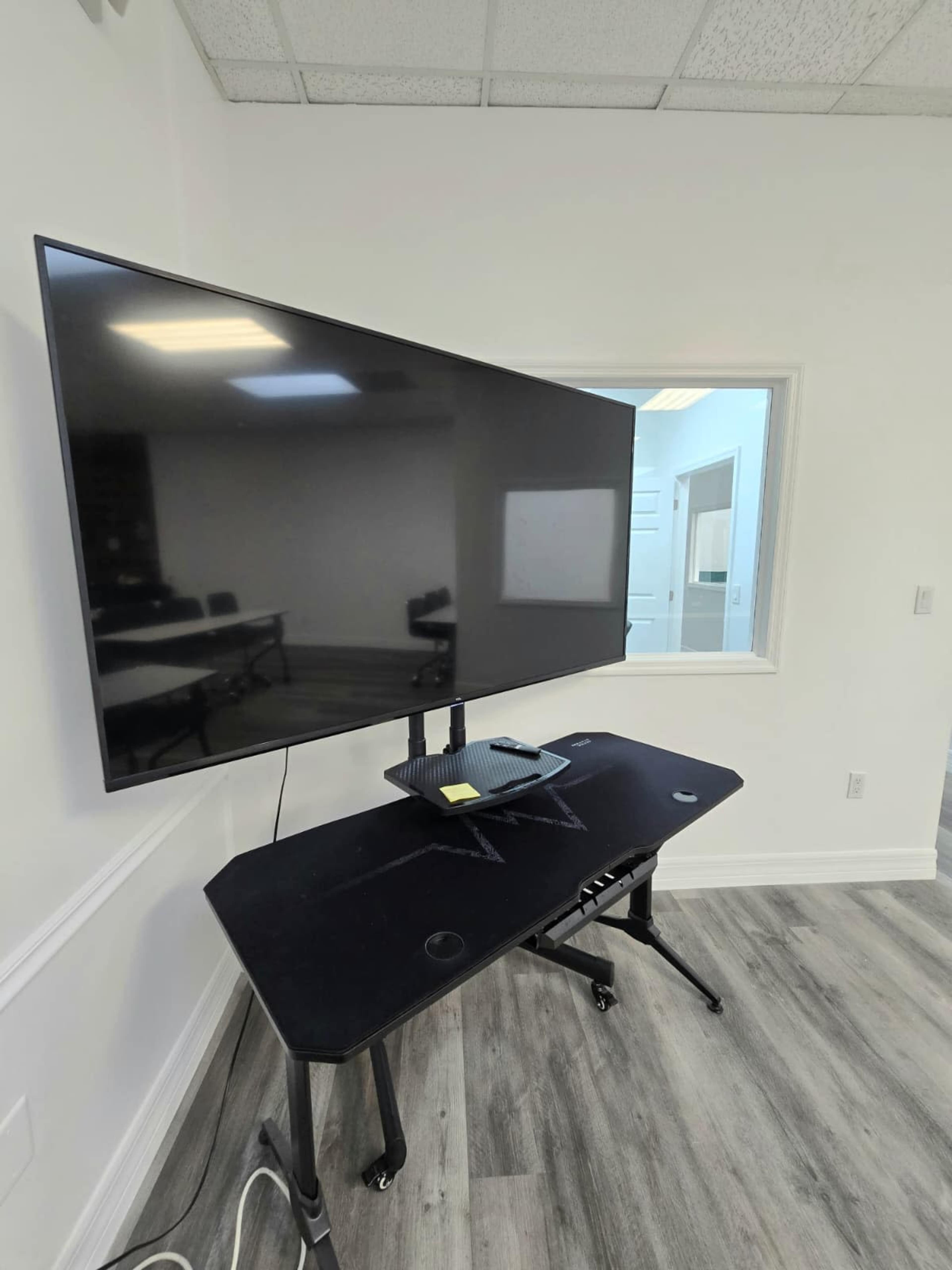 A large television is mounted on a desk in a bright room with a window.