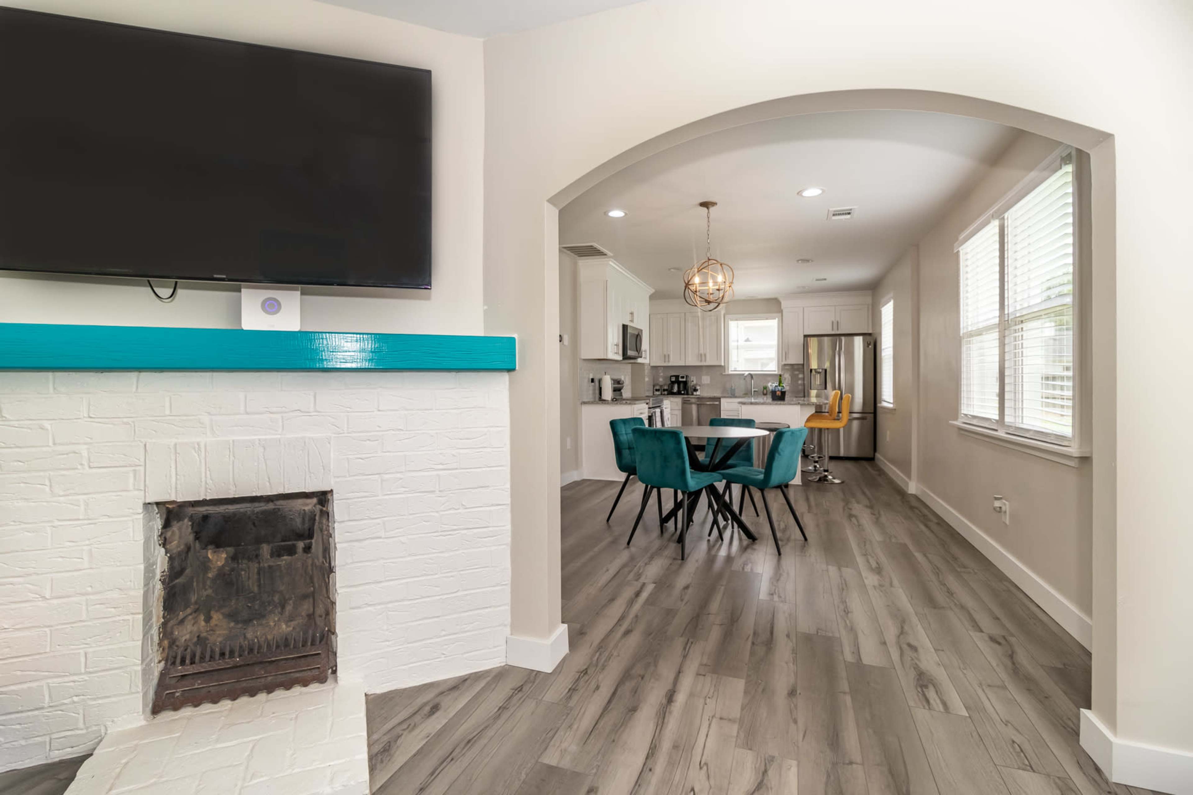 A modern living space featuring a white brick fireplace, a large TV mounted on the wall, and a dining area with a round table and colorful chairs.