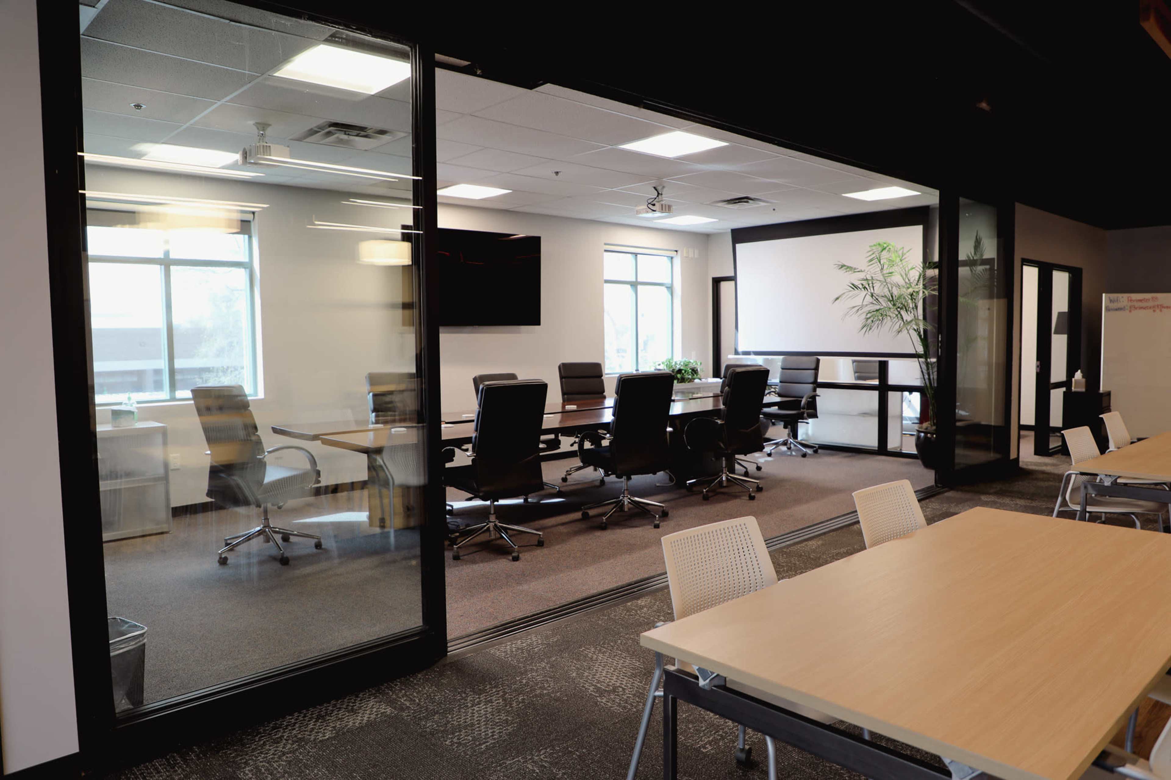 A modern conference room with a large table and black chairs is visible through a glass wall, adjacent to a more casual seating area with tables.