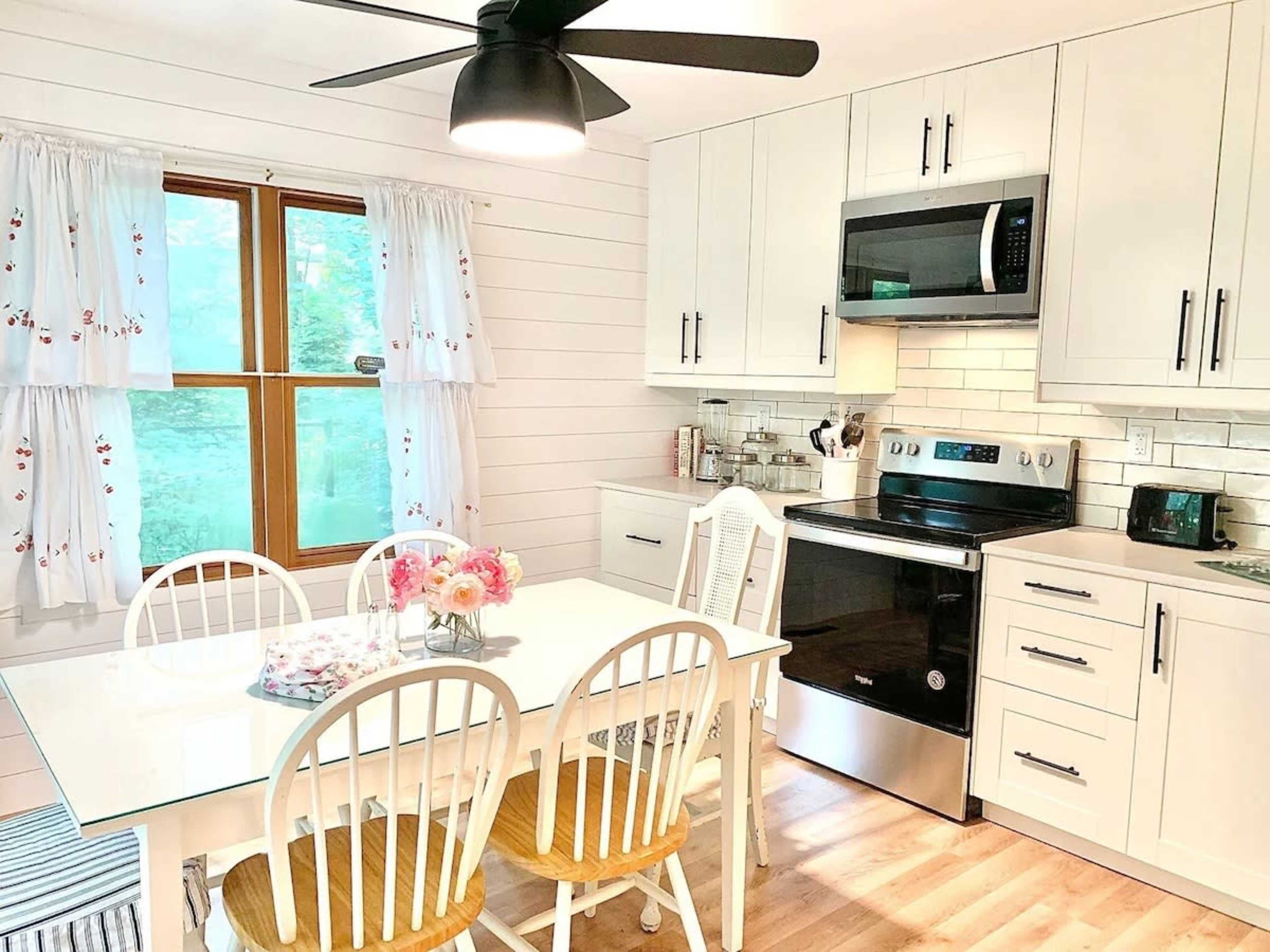 A modern kitchen features white cabinets, a stainless steel microwave and oven, and a dining table with white chairs.