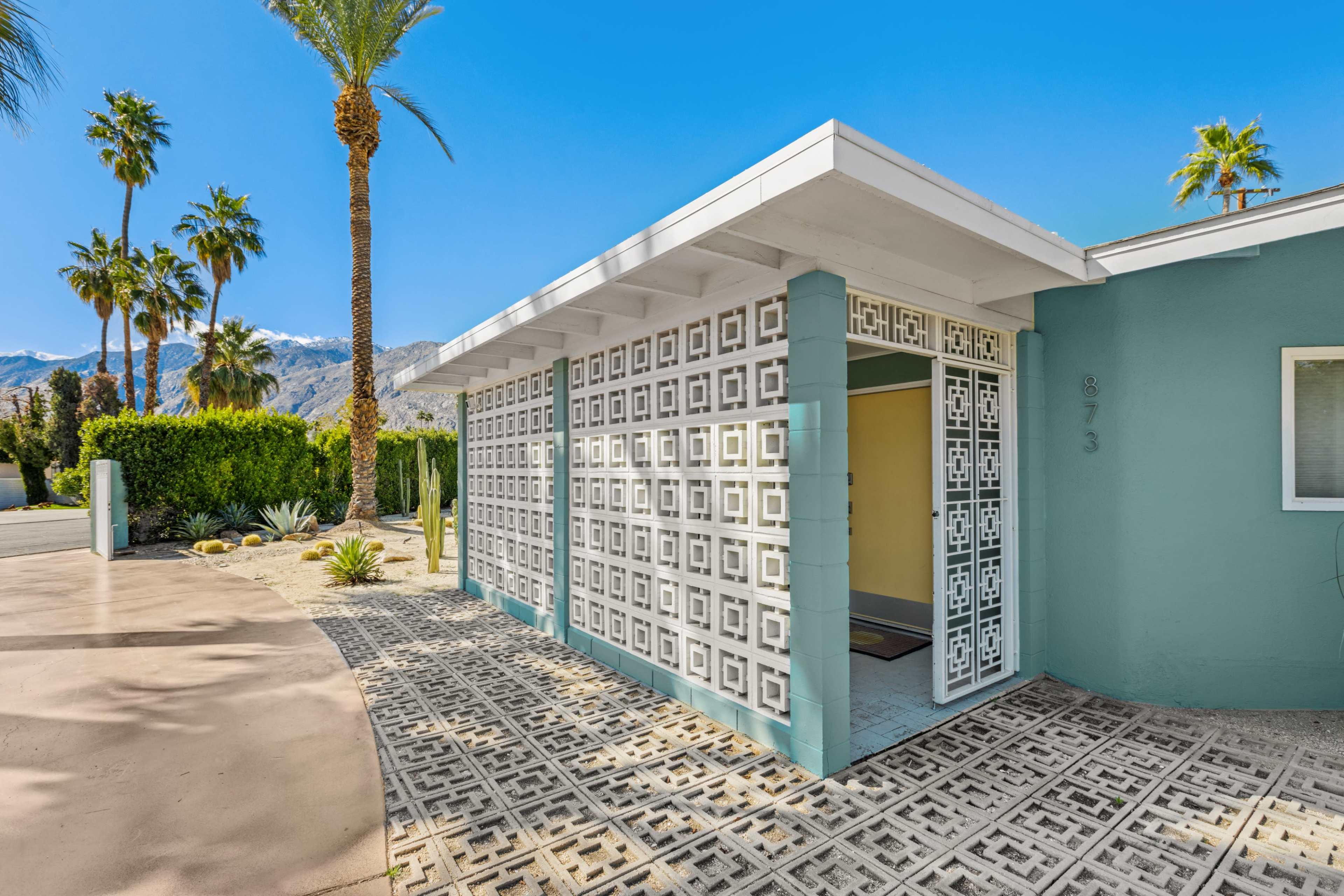 A modern house entrance with patterned concrete walls and palm trees in the background.