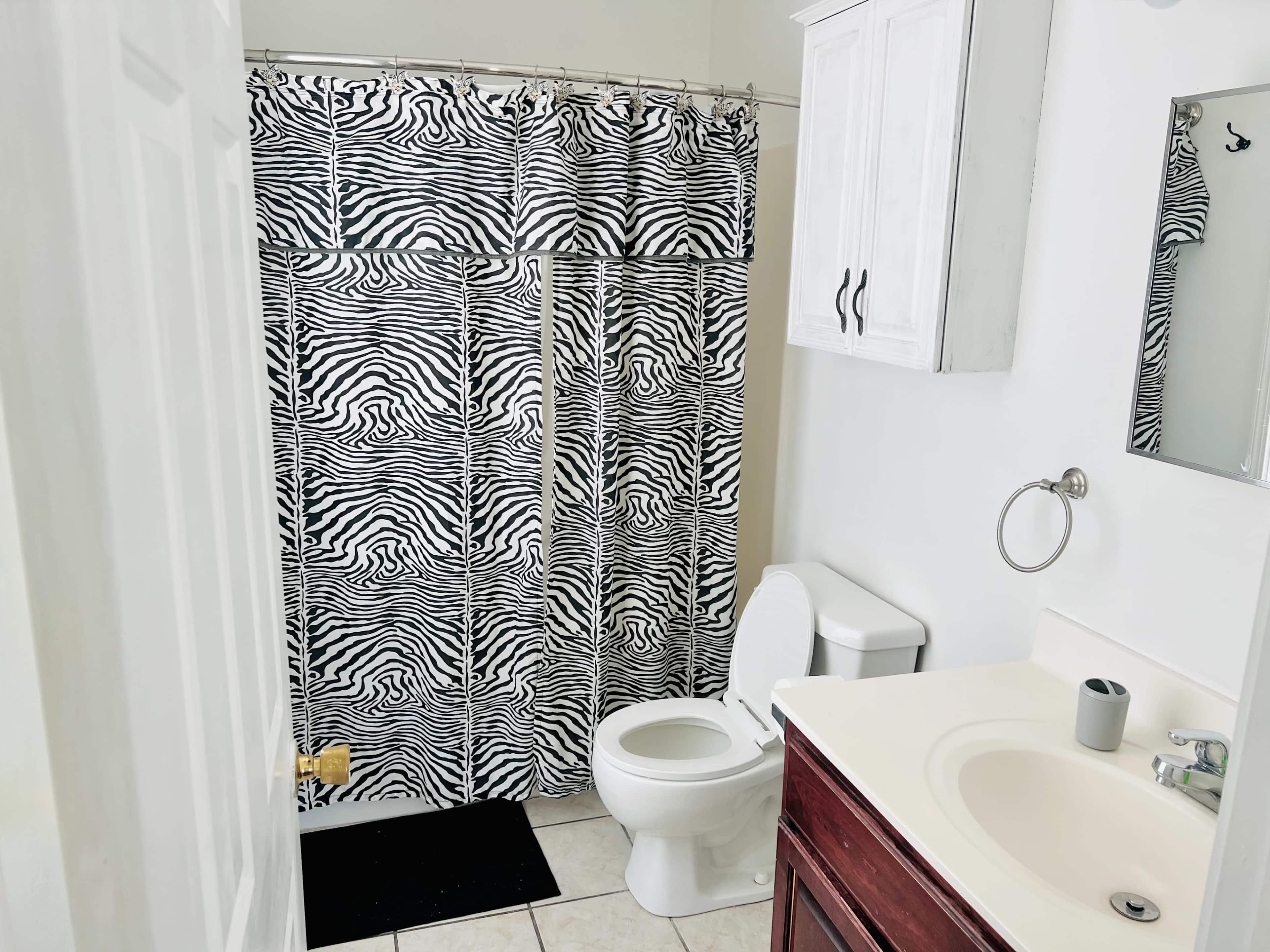 The bathroom features a zebra-patterned shower curtain, a toilet, and a sink with a wooden cabinet below.