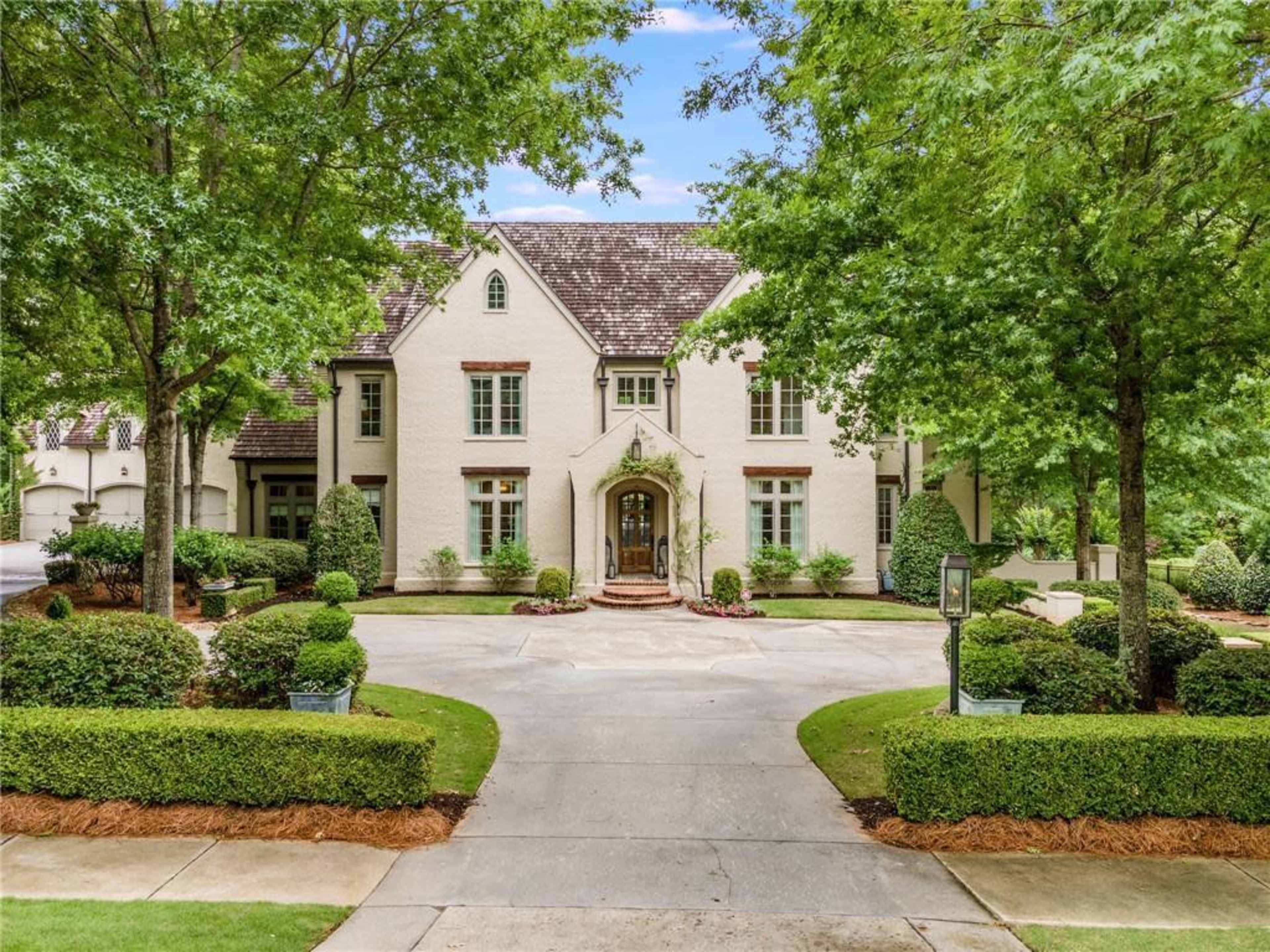 A large, two-story white house surrounded by neatly trimmed greenery and a circular driveway.