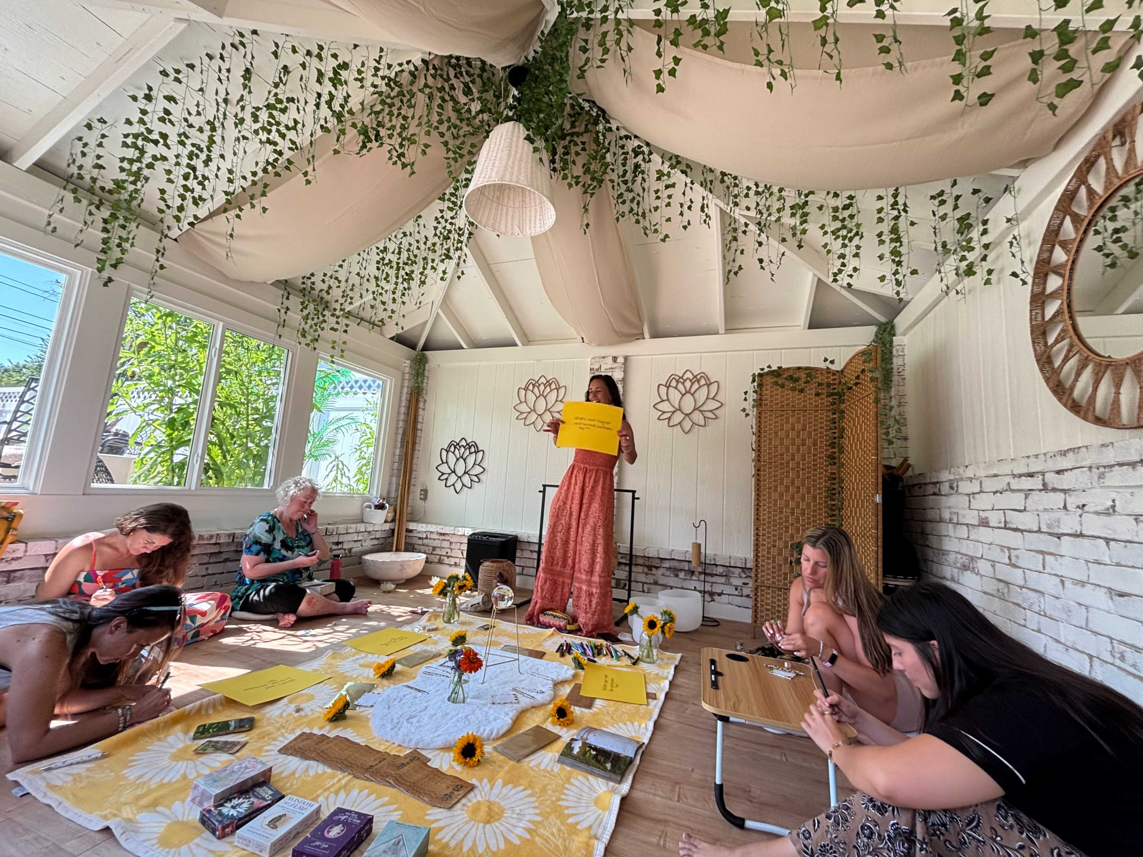 A group of people engage in a creative activity in a well-decorated room adorned with plants and sunflowers.