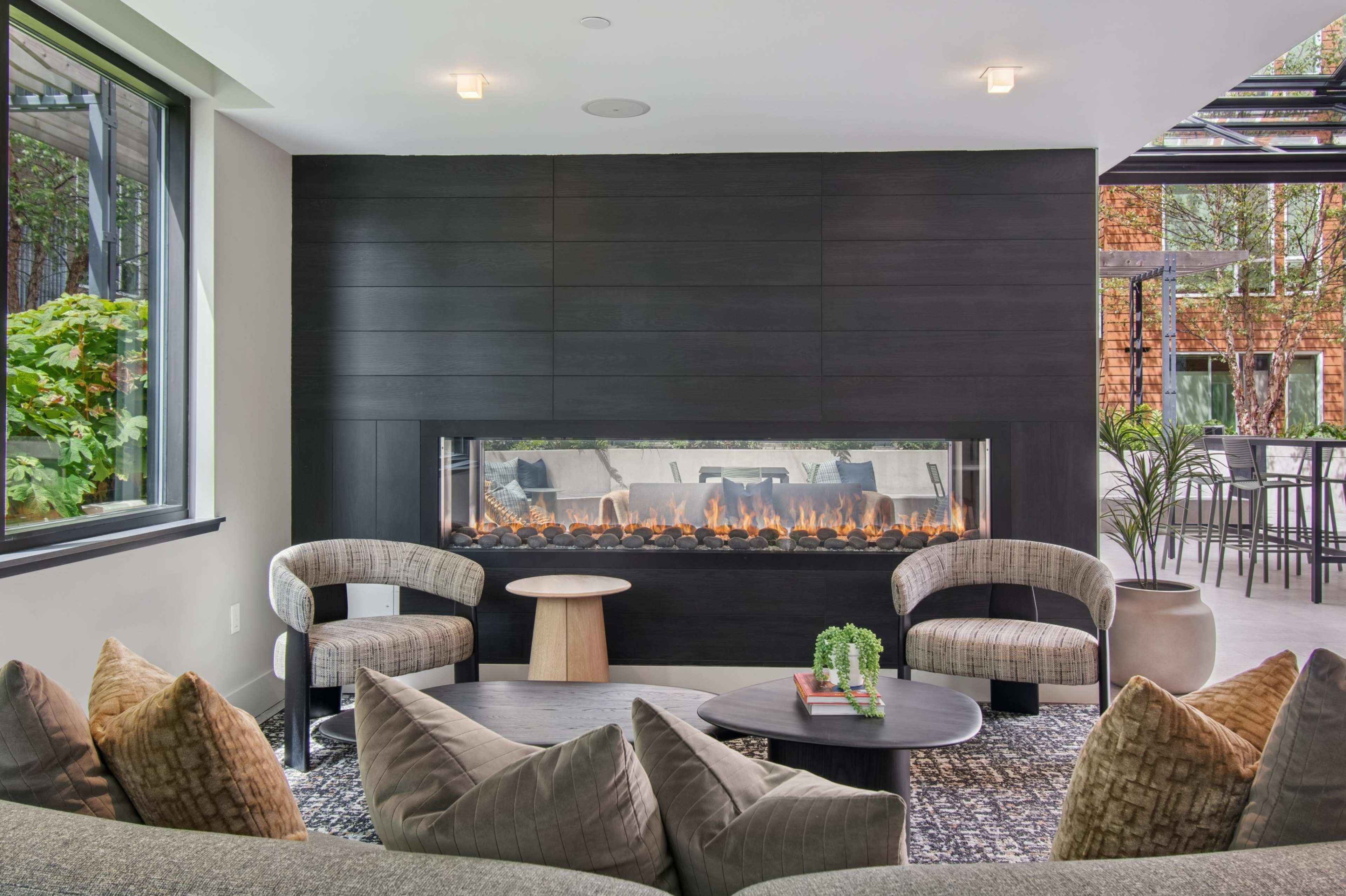 The image shows a modern living space featuring a sleek, linear fireplace against a black wall with two contemporary chairs and a low table arranged in front of it.