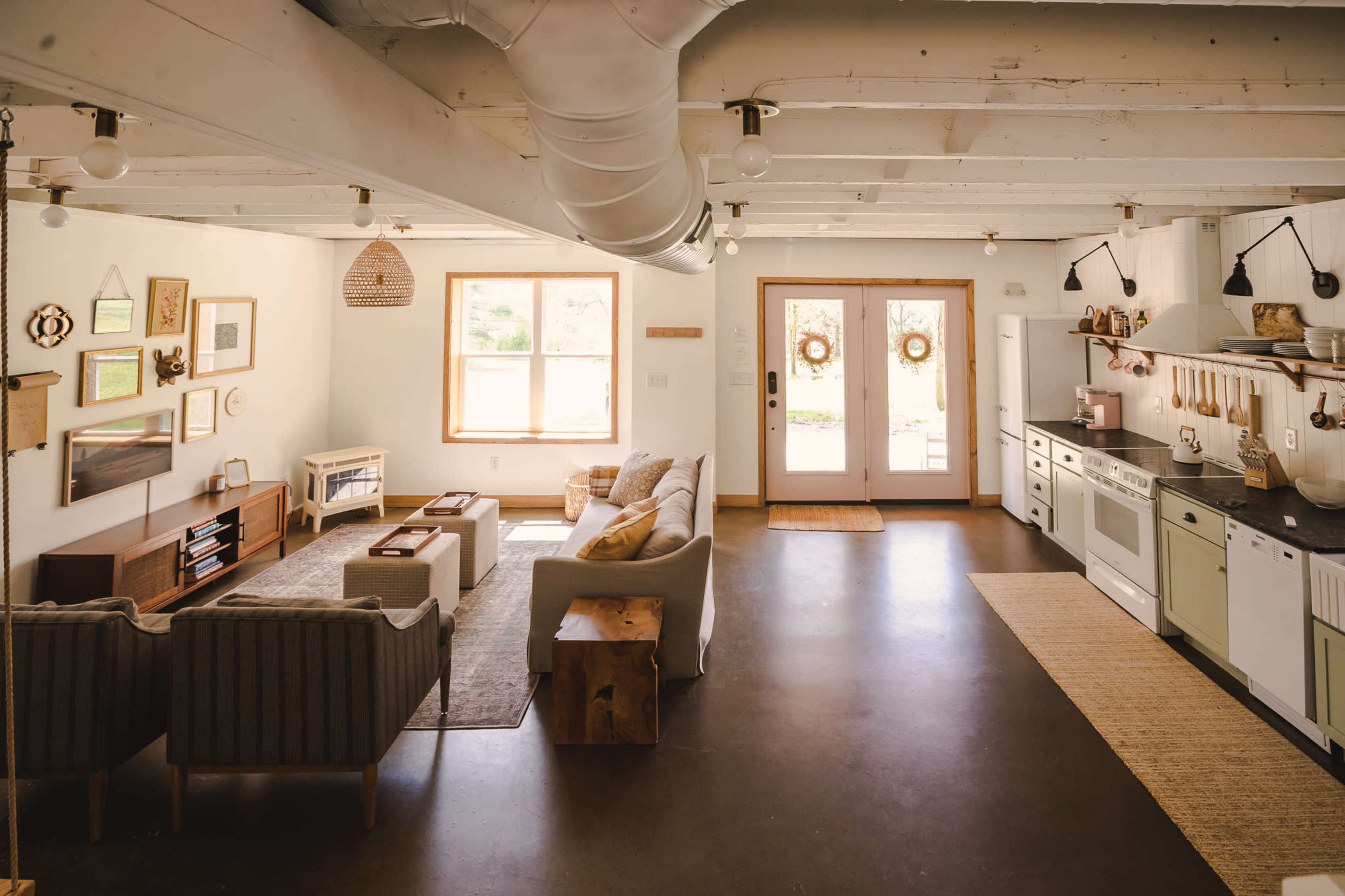 A spacious, light-filled living area features a seating arrangement with a sofa and chairs, a wooden coffee table, and an open kitchen with modern appliances.