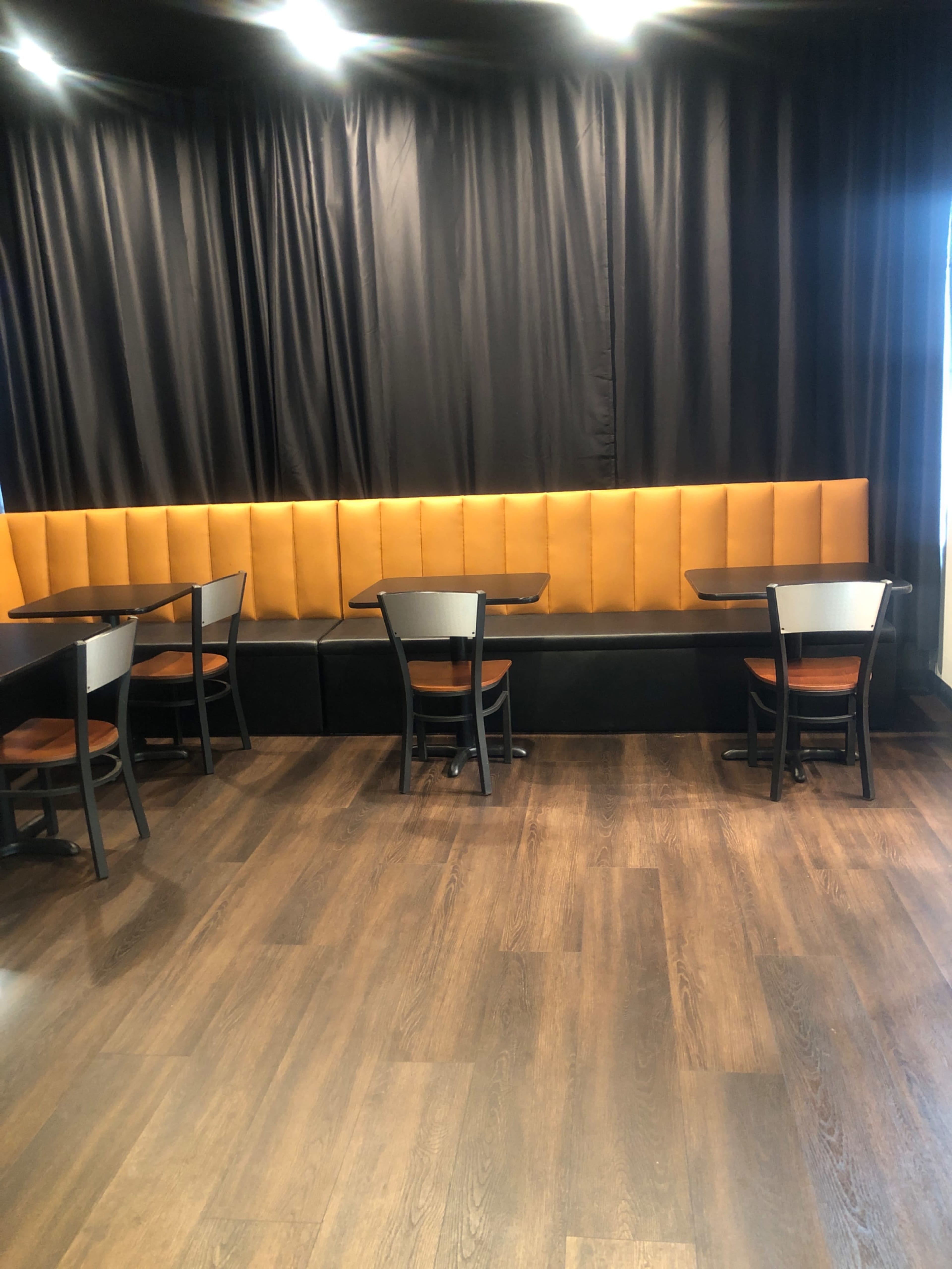 The image shows a dining area with black walls, orange cushioned seating along one side, and several small tables and chairs arranged in the space.