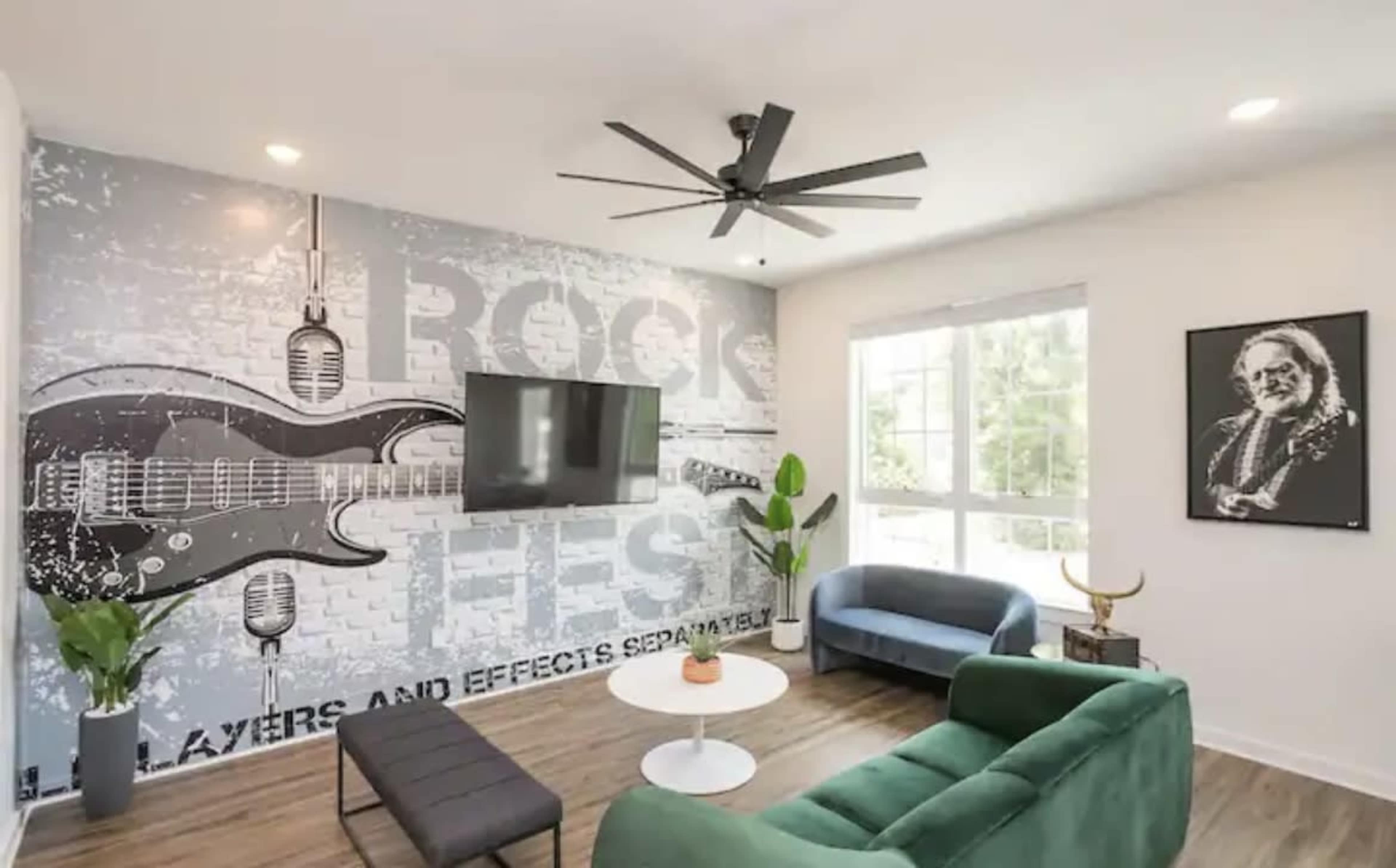 A living room featuring a large guitar mural, a mounted TV, a green couch, and a black coffee table.