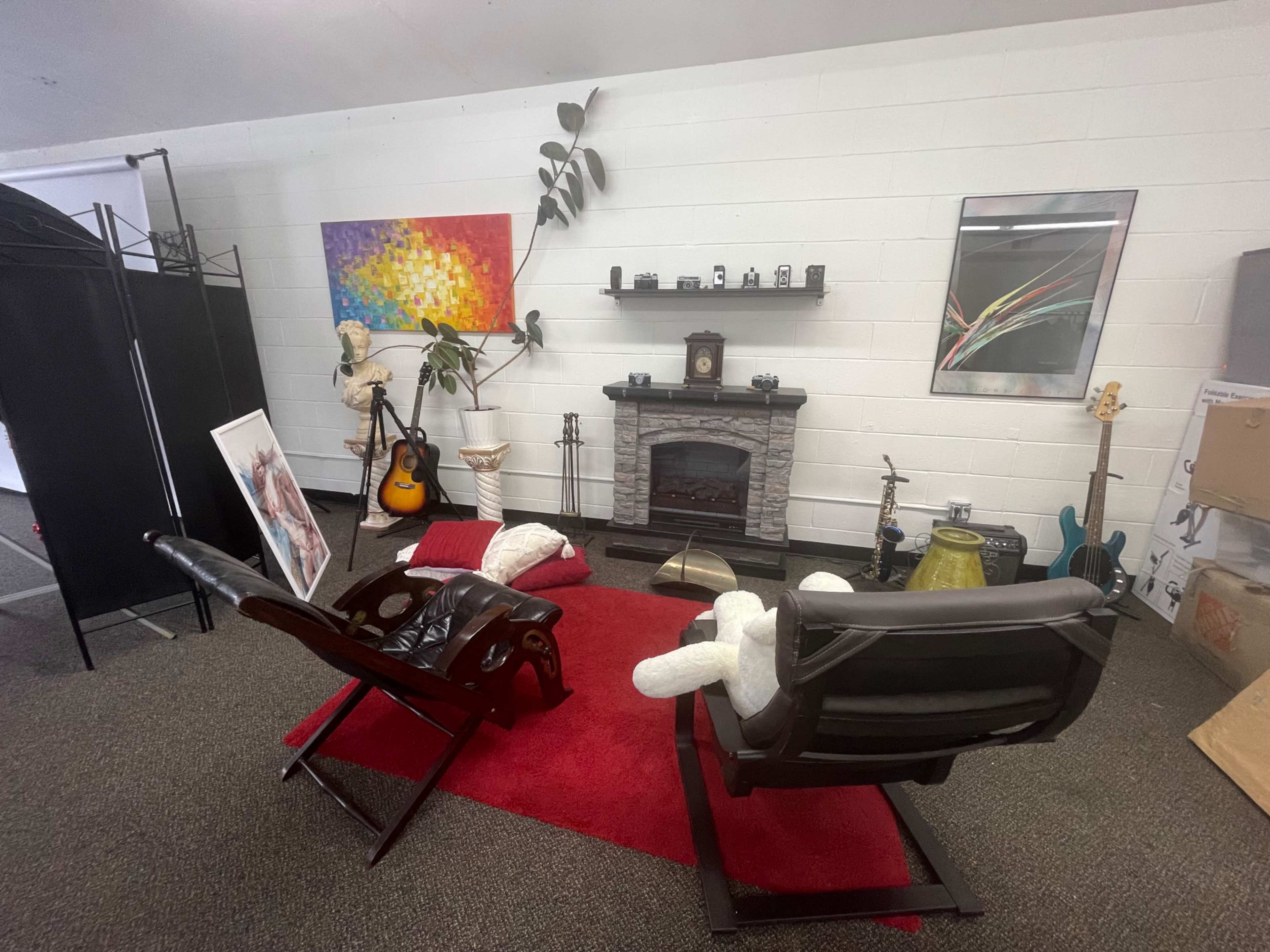 The scene features a cozy room with two chairs facing a stone fireplace, surrounded by various artworks, musical instruments, and decorative items.