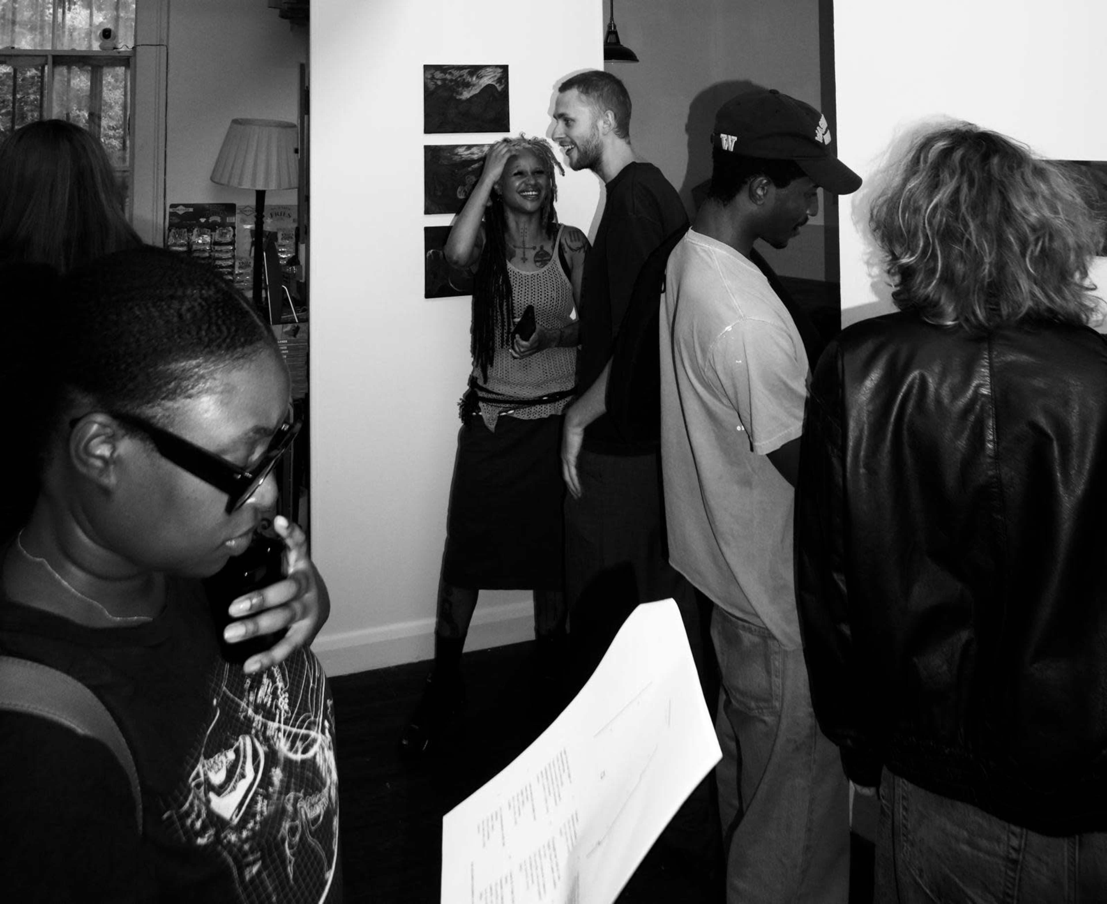 A group of people converse and interact in an art gallery setting, surrounded by artwork on the walls.