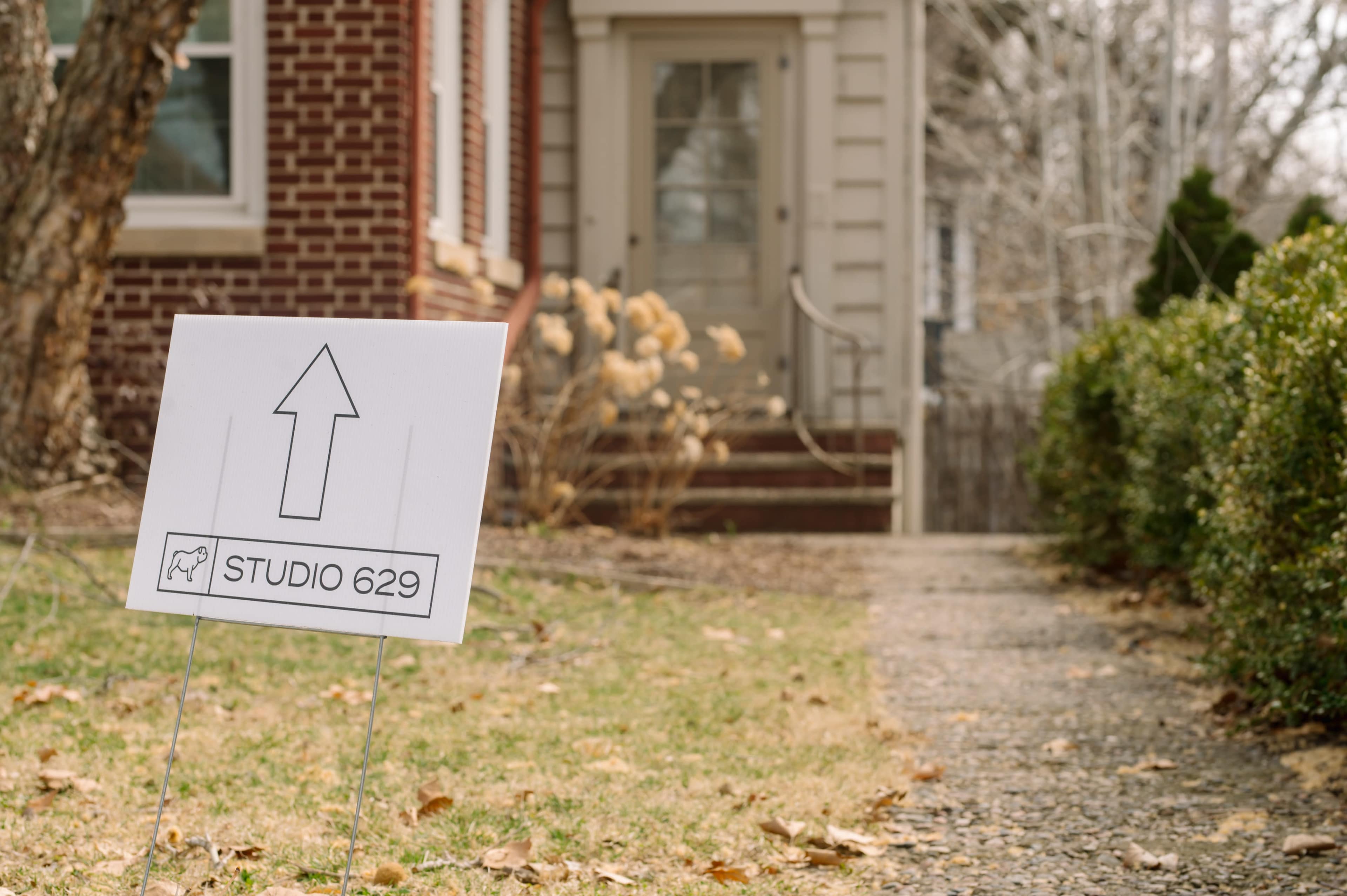 A sign labeled "STUDIO 629" with an arrow is positioned in a yard leading to a brick house.