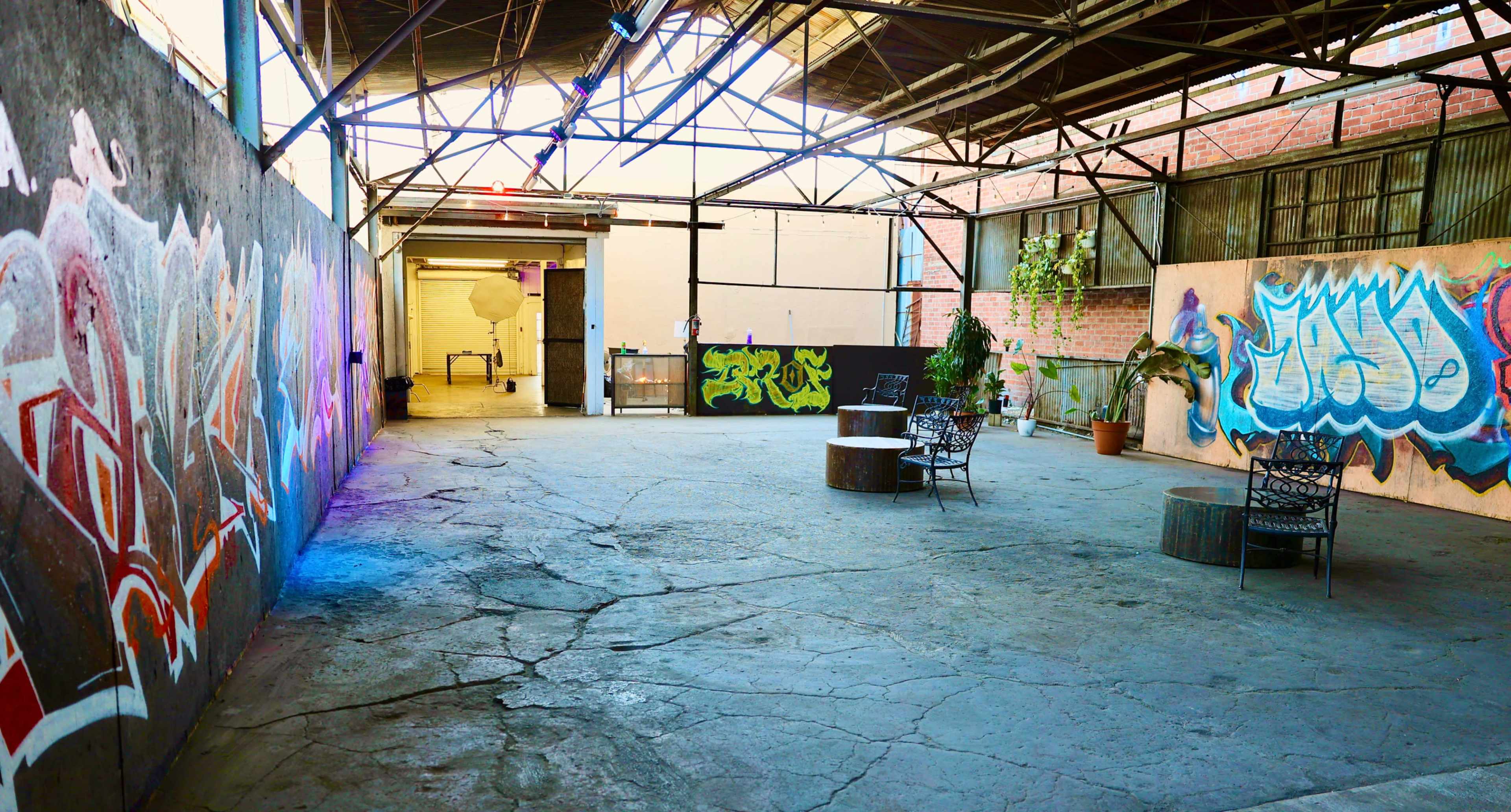 The image shows an open, graffiti-adorned warehouse space with two seating areas surrounded by concrete flooring and exposed beams.