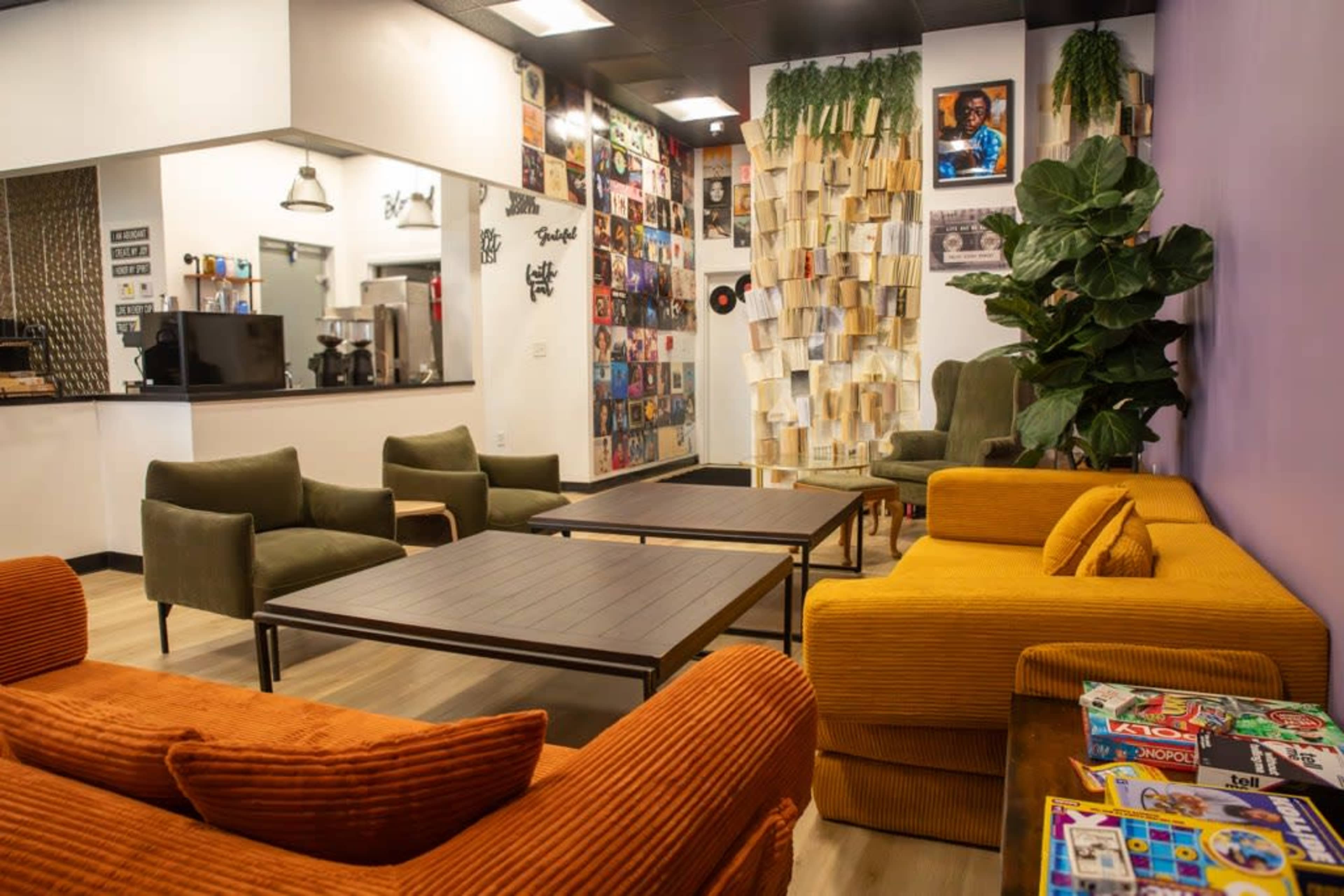 The image shows a cozy lounge area with green and orange sofas, a coffee table, and a wall adorned with records and photos.