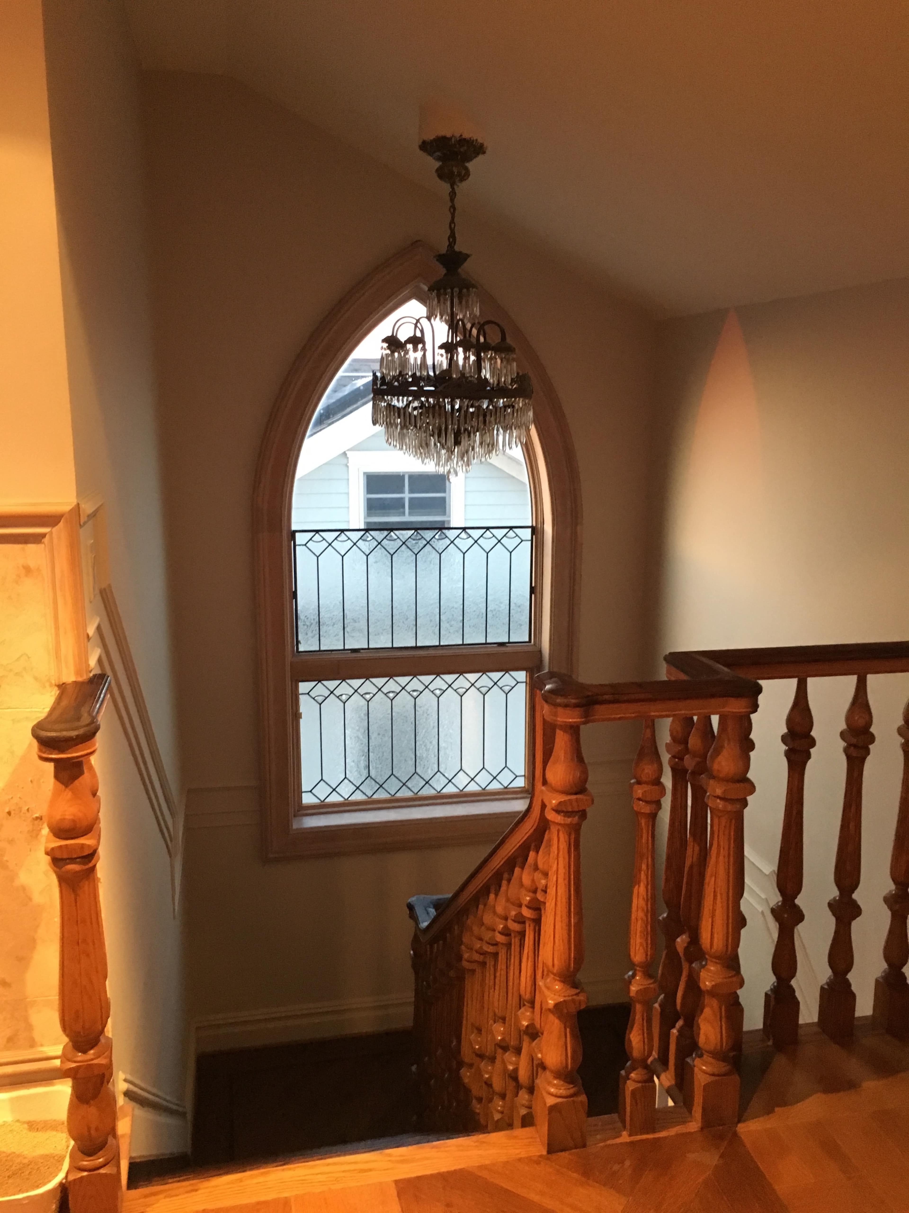 A staircase with a wooden railing leading to a window featuring an arched design and a chandelier above.