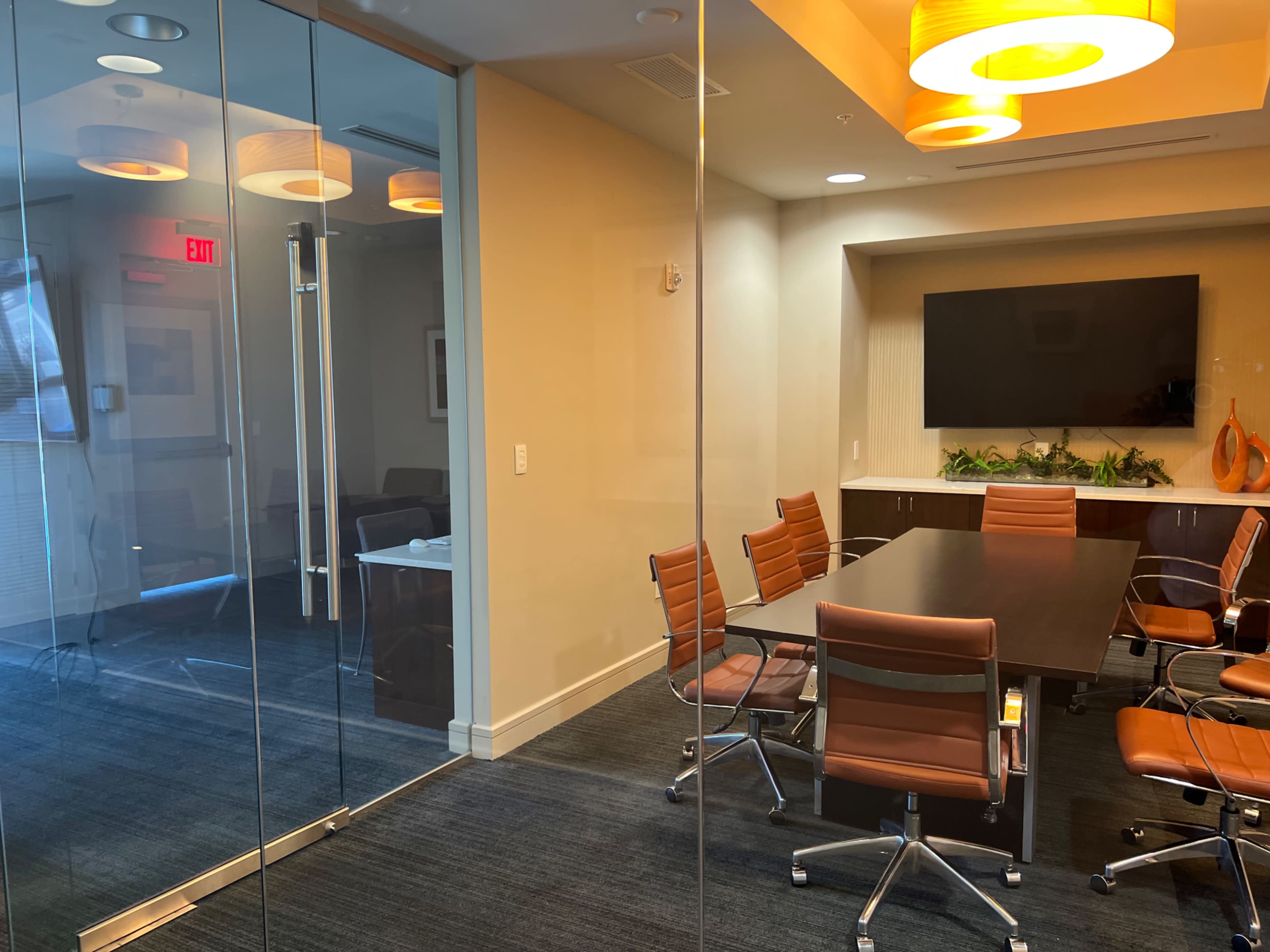 A modern conference room features a large table surrounded by ergonomic chairs, with a glass wall that separates it from an adjacent space.