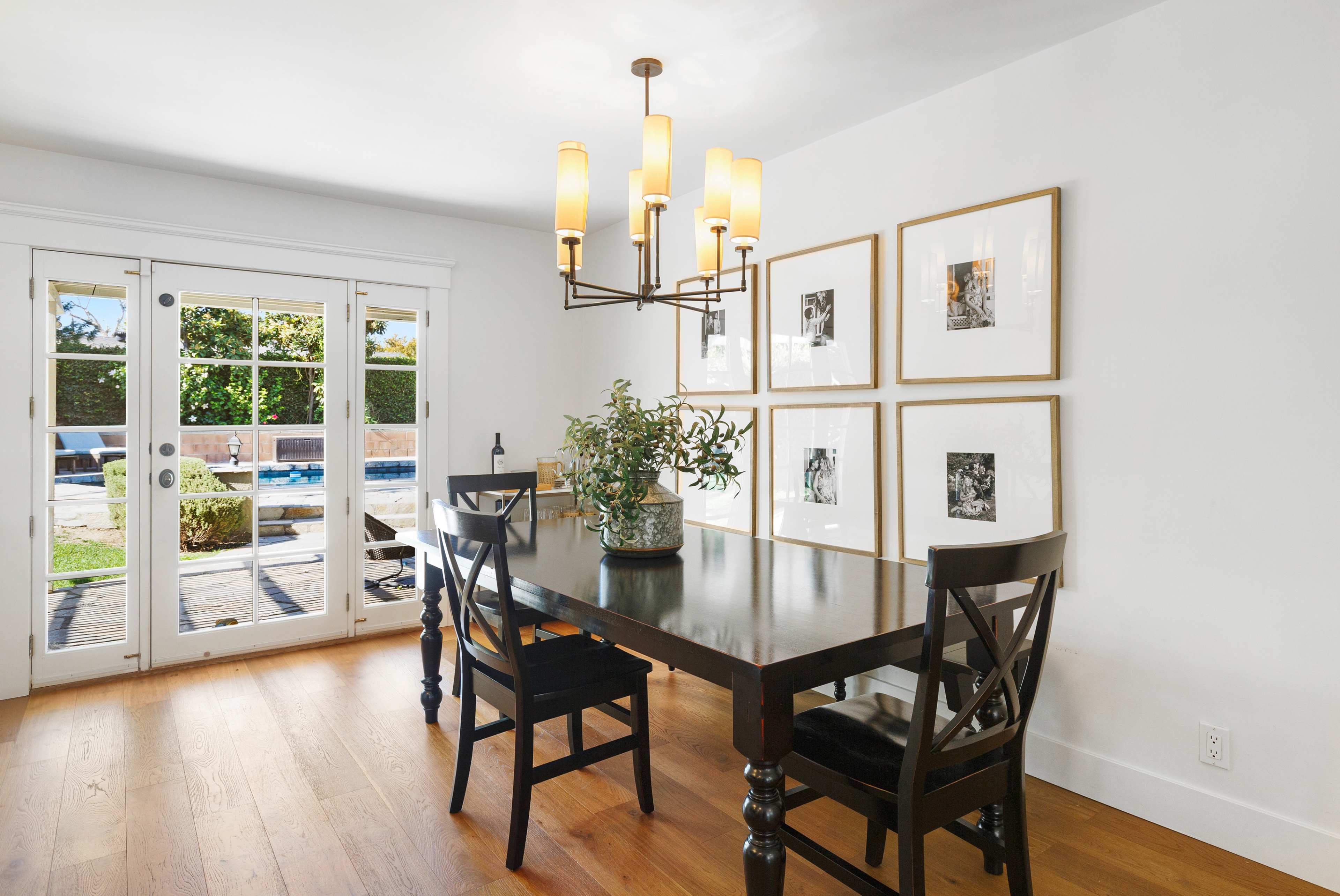 A dining area features a black table and chairs, surrounded by framed pictures, with glass doors leading to a poolside patio.
