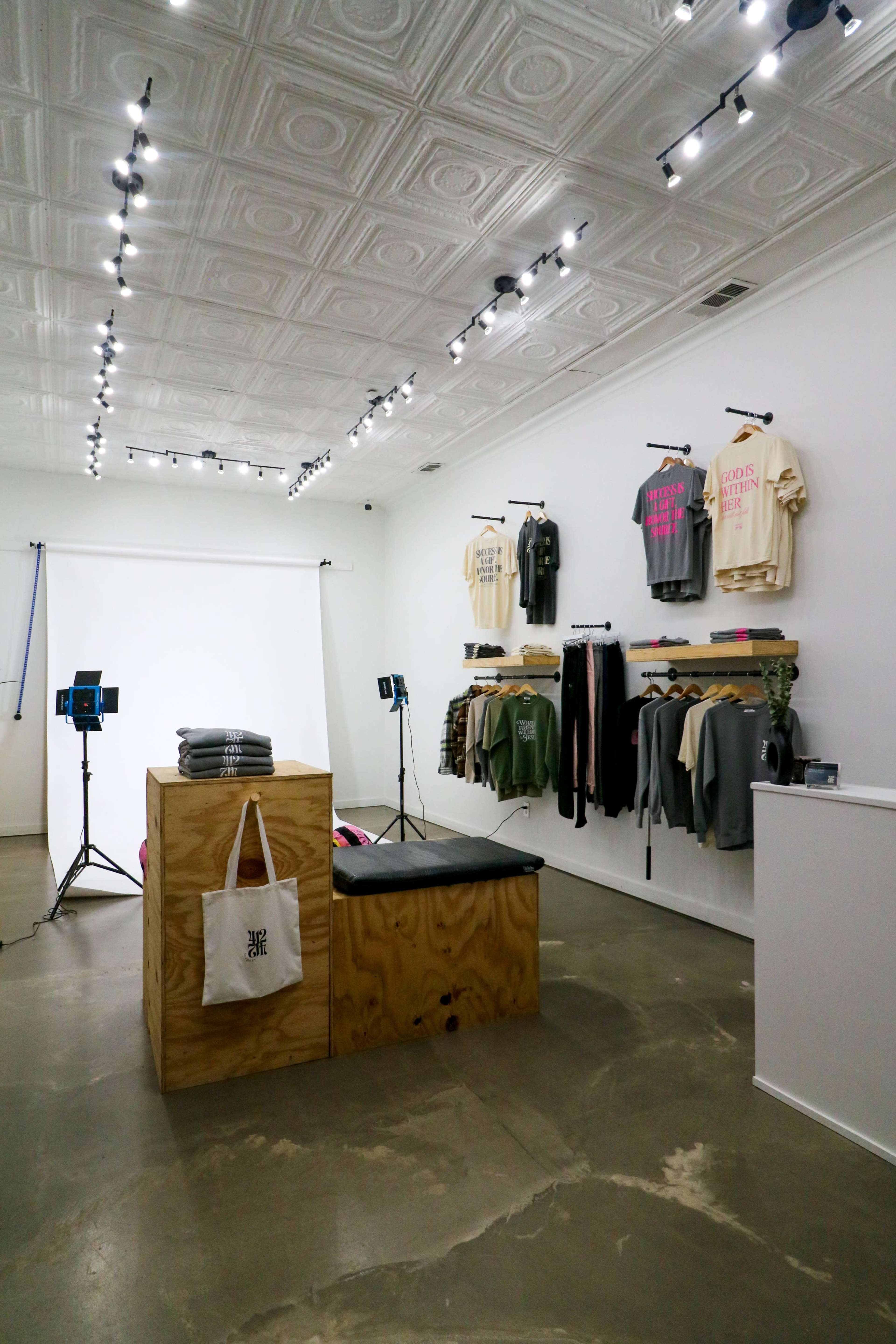 A modern retail space features a displayed collection of clothing on the walls, with a minimalist wooden display and bright lighting.