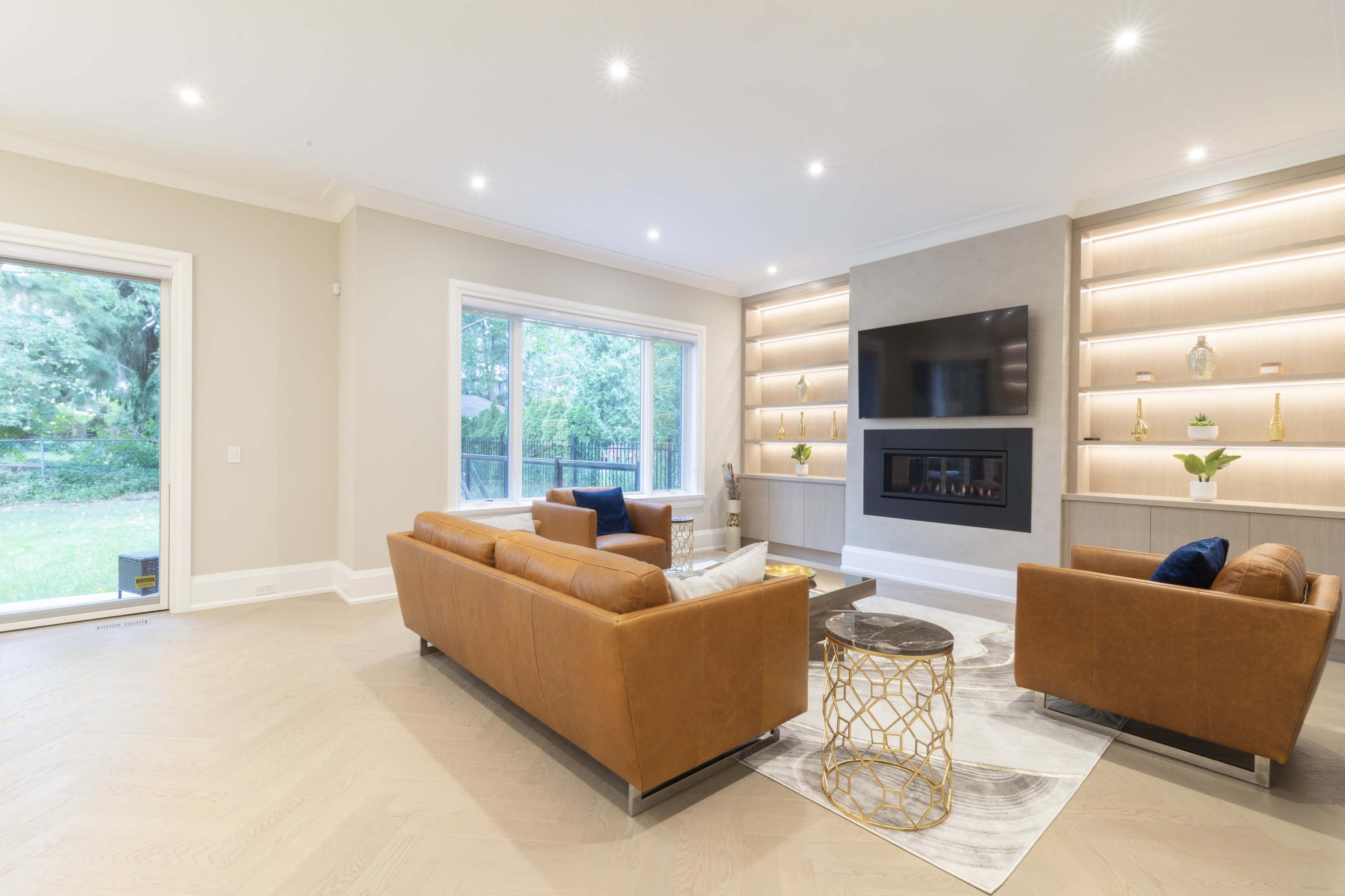 A well-lit living room features two brown leather sofas, a marble coffee table, and a modern entertainment unit with built-in shelves.